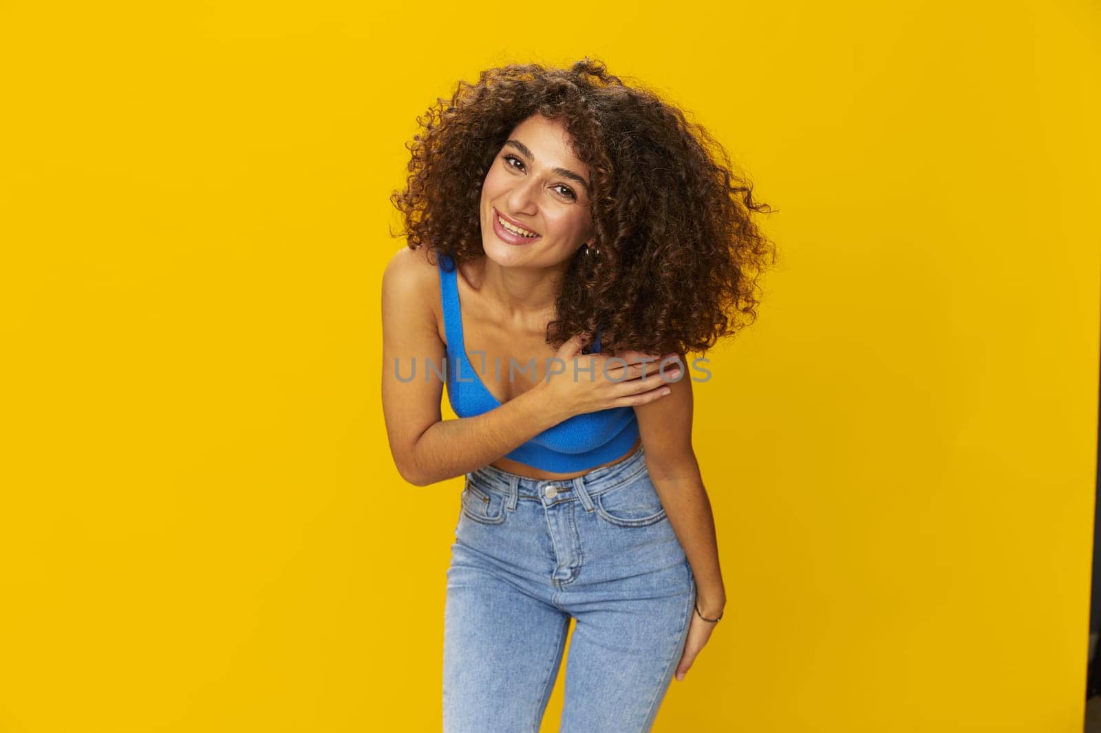 Woman with curly afro hair in a blue t-shirt on. yellow background signs with her hands, look into the camera, smile with teeth and happiness, copy space. High quality photo