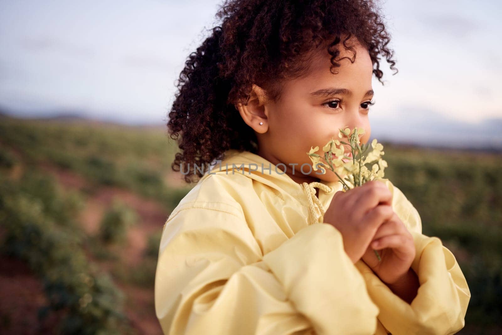 Children, farm and a girl smelling a flower outdoor in a field for agriculture or sustainability. Kids, nature and spring with a female child holding flowers to smell their aroma in the countryside.