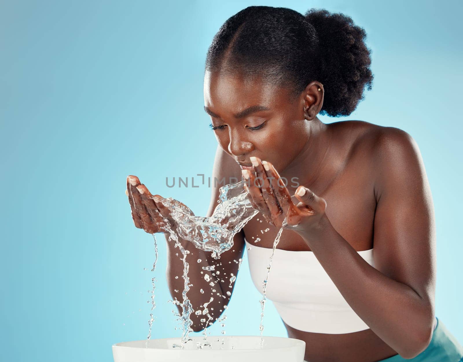 Water, wash and woman splashing her face for cleansing hygiene and skincare on a blue studio background. Skin care, body care and beauty female washing her for facial health and wellness.