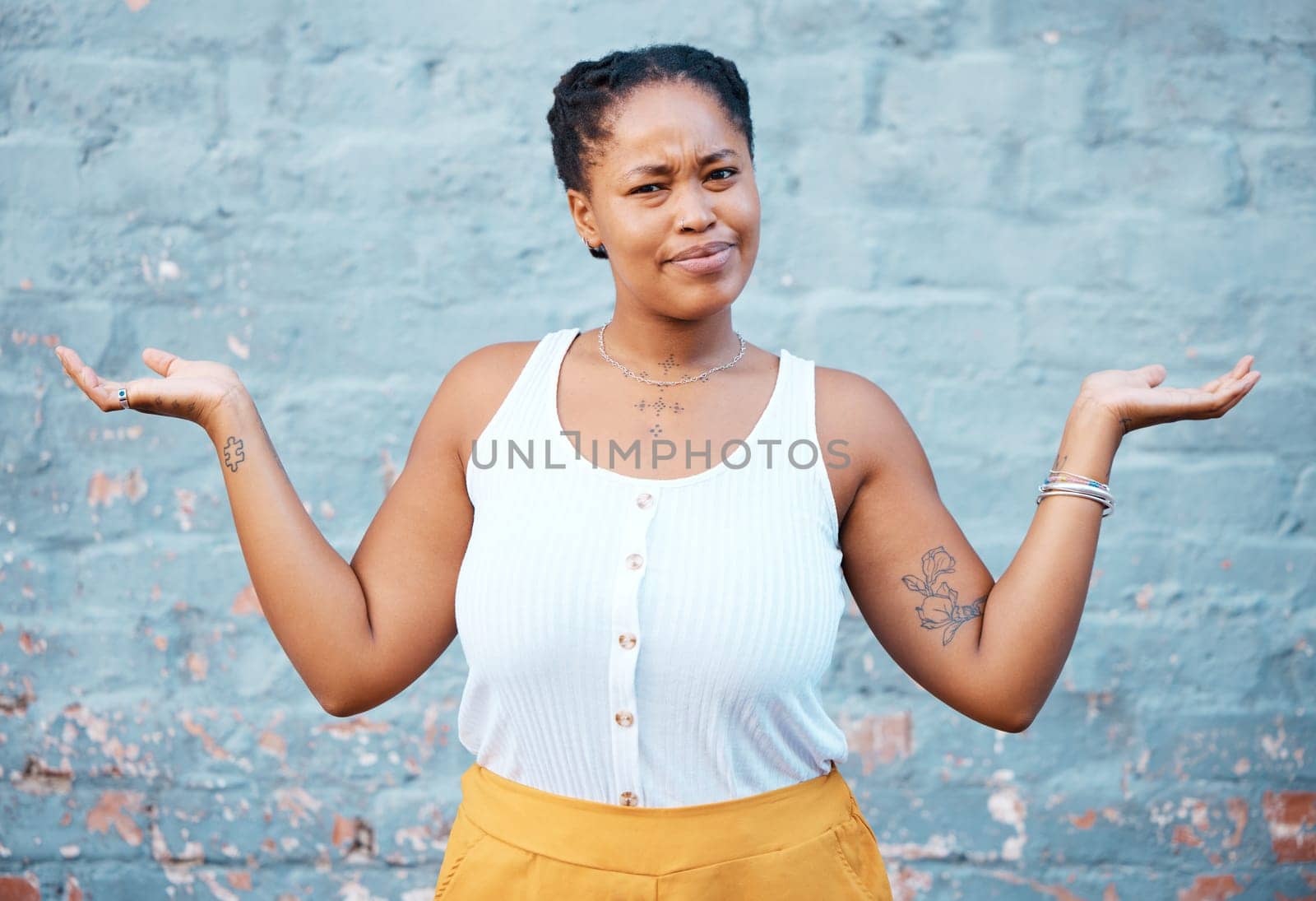 Portrait of confused black woman in doubt with a question and unsure gesture with arms up. Asking why, confusion and clueless girl with hands raised standing by a wall outside in urban town or city.
