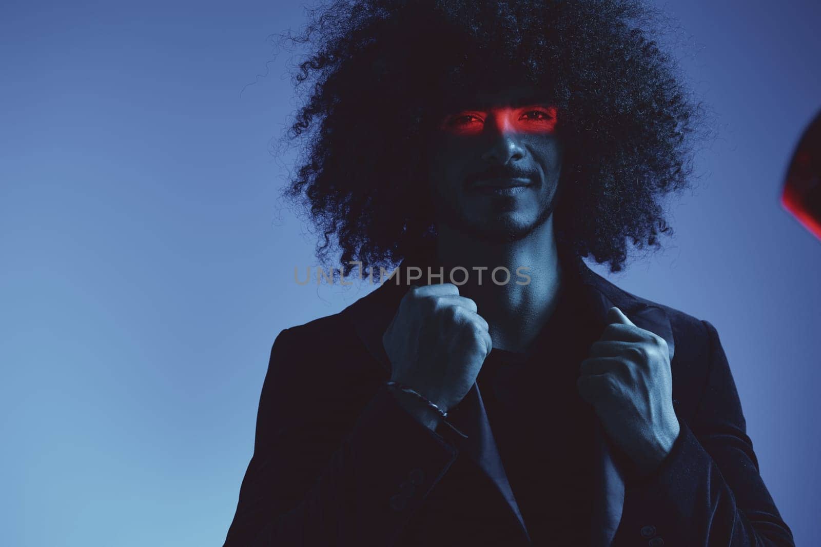 Fashion portrait of a man with curly hair on a blue background with a red stripe of light, multicolored light, trendy, modern concept. High quality photo