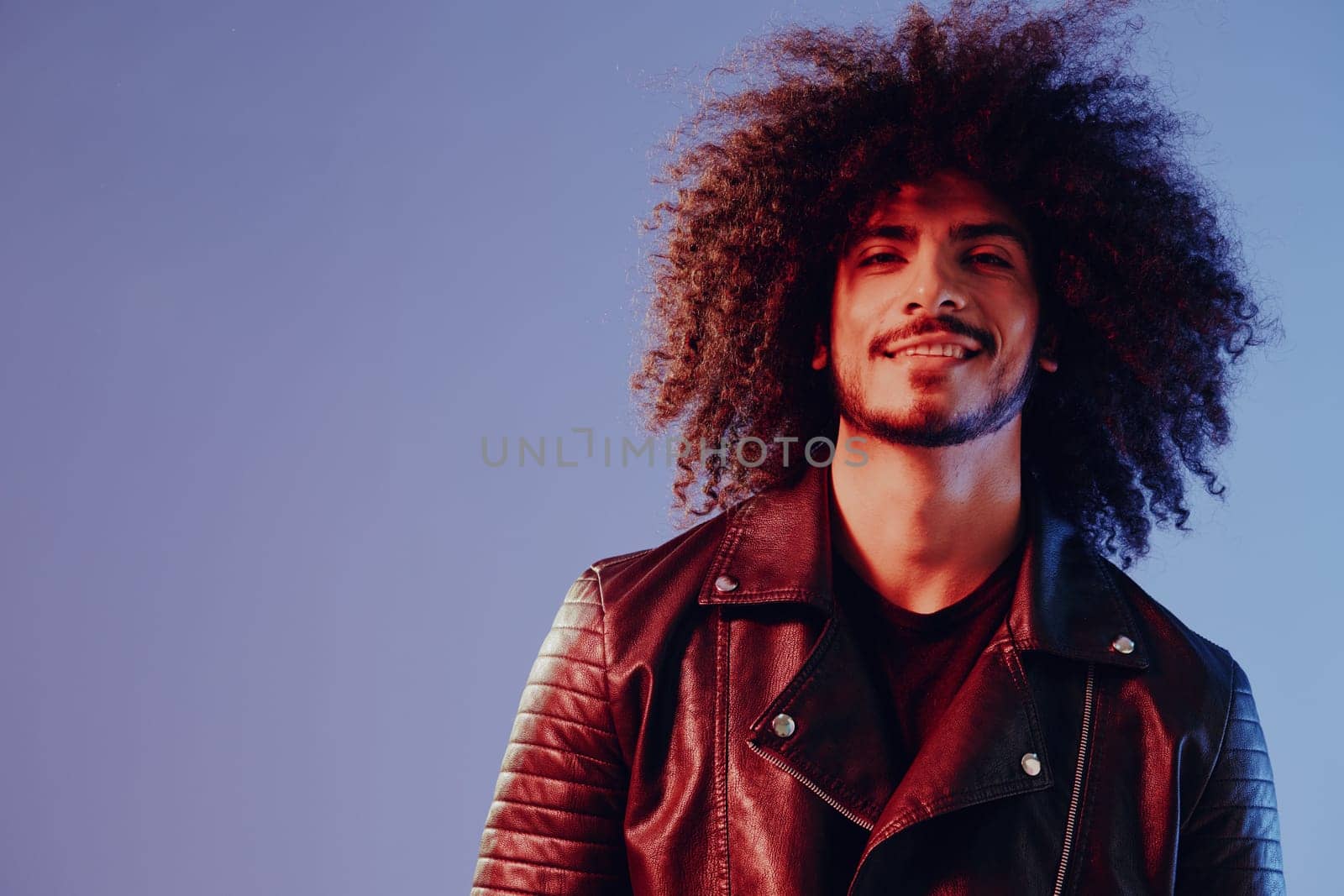 Portrait of a stylish man with curly hair with glasses smile on blue background multinational, color light, black leather jacket trend, modern concept. High quality photo