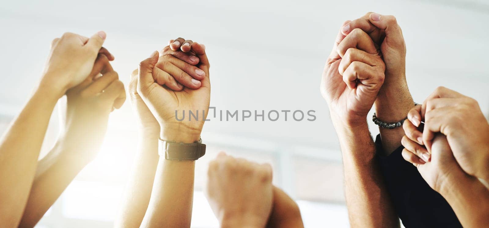 Closeup shot of a group of unrecognizable businesspeople holding hands while raising their arms.