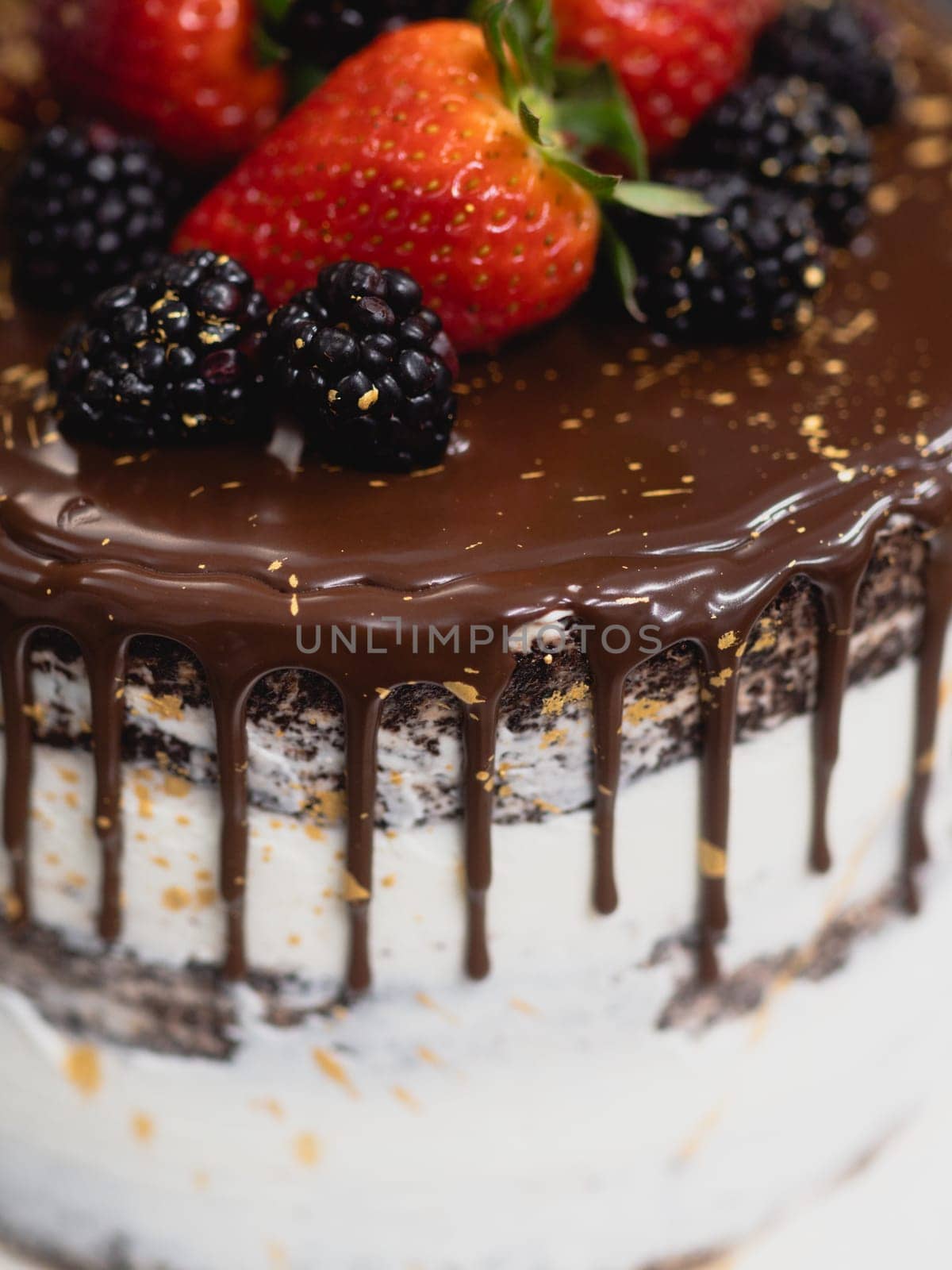 pastry chef preparing a chocolate frosted dripped icing cup cake with sweet fruit topping and golden brush strokes