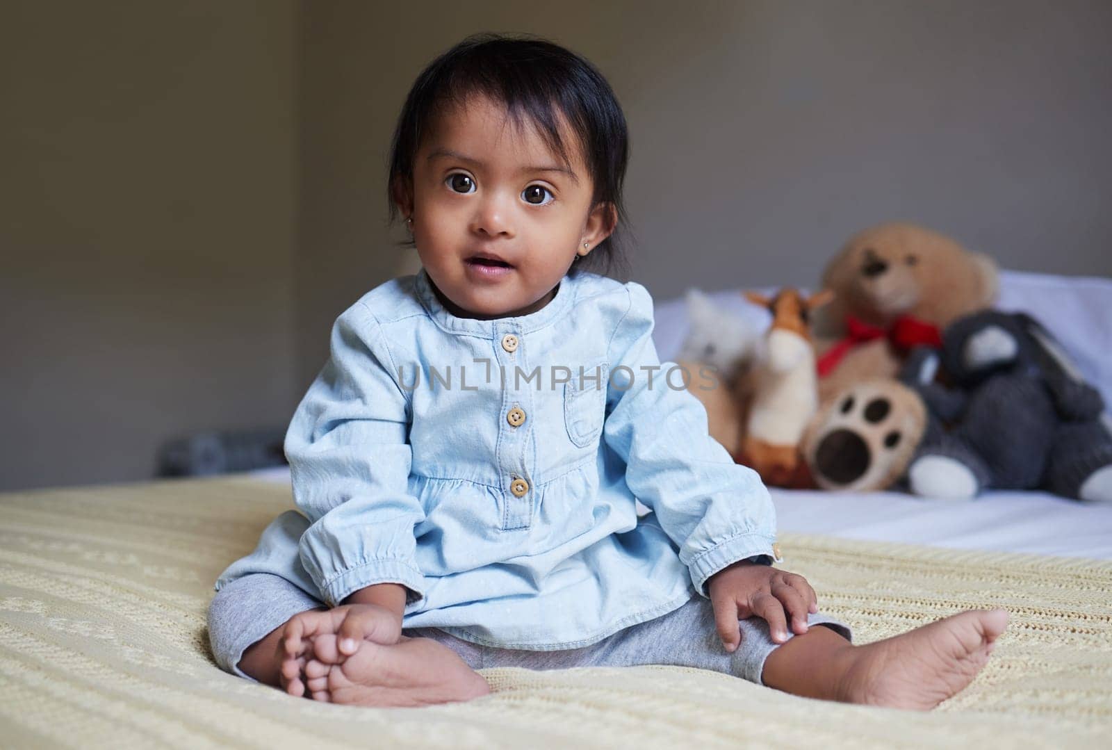 Baby, cute and innocent with a girl on a bed in her home alone with a teddy bear and stuffed toys in the background. Children, small and pure with a female kid in her bedroom in a house in India by YuriArcurs