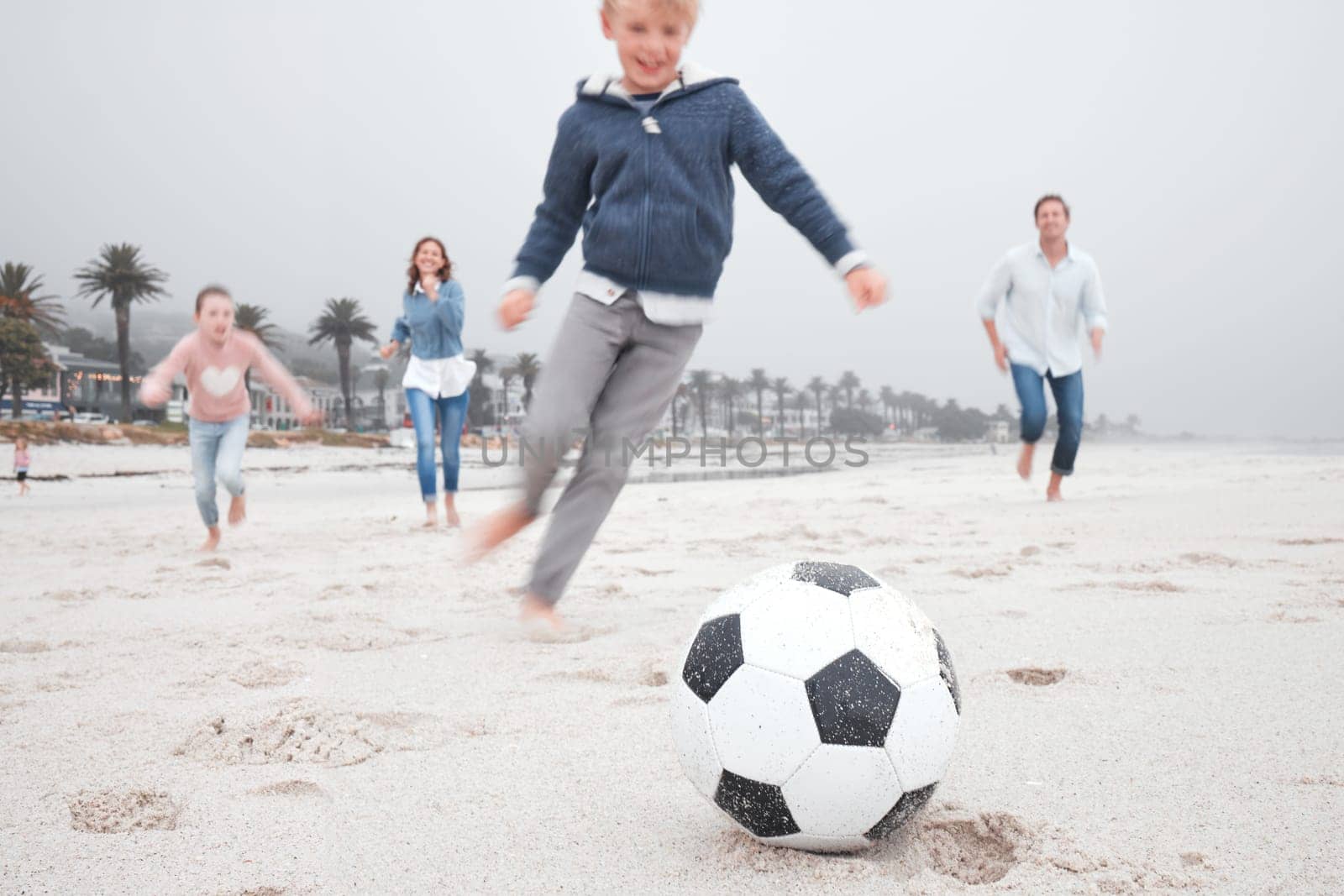 Family, soccer and beach playing on sand together for fun bonding time for sports and exercise in nature. Happy children and parents in playful fitness for football game on a sandy ocean shore by YuriArcurs