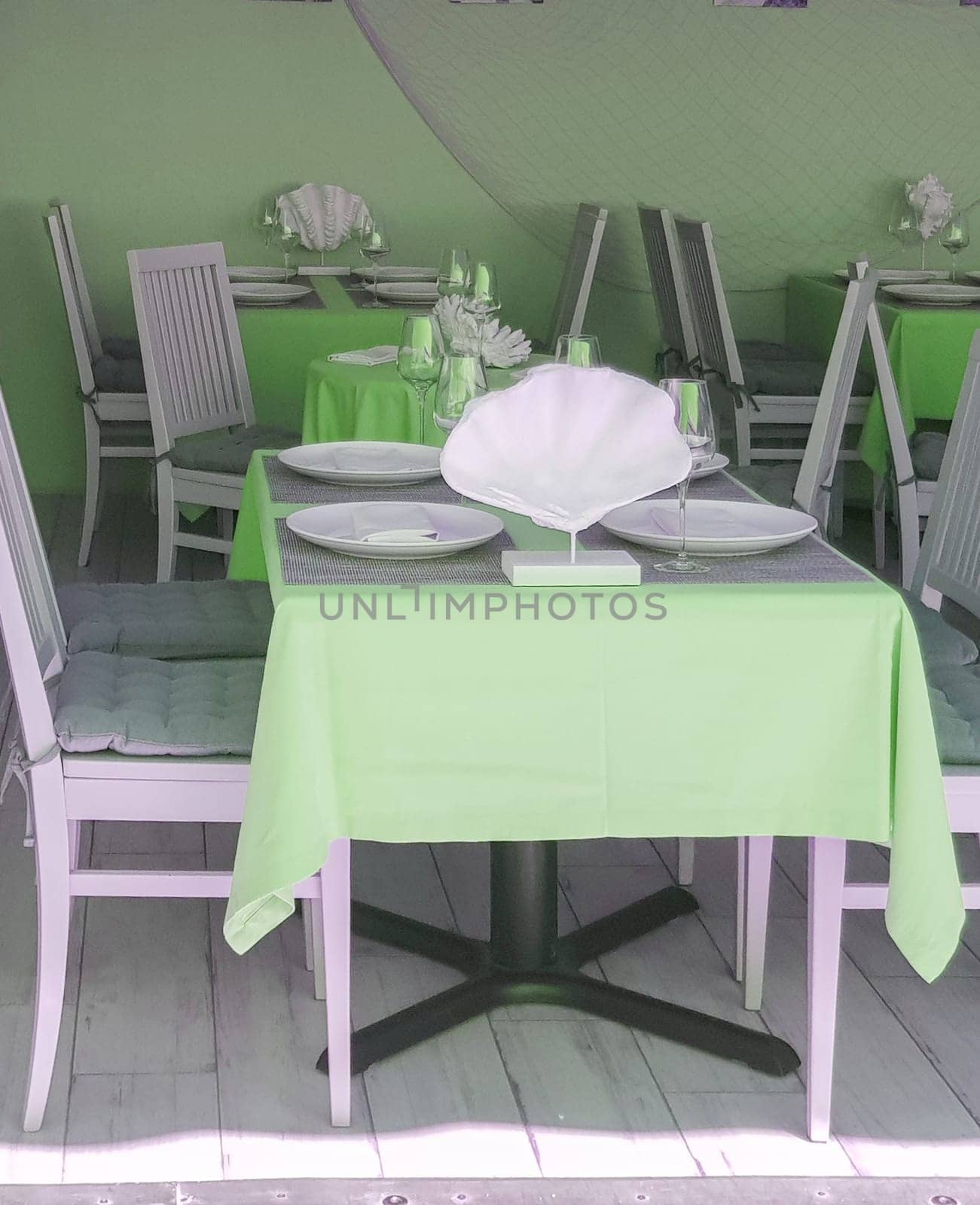 Beautiful table setting with glasses, tablecloth, plates in a nautical style in a fish restaurant, green tinting.