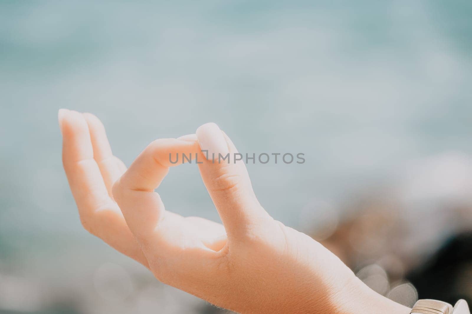 Close up Yoga Hand Gesture of Woman Doing an Outdoor meditation. Blurred sea background. Woman on yoga mat in beach meditation, mental health training or mind wellness by ocean, sea by panophotograph