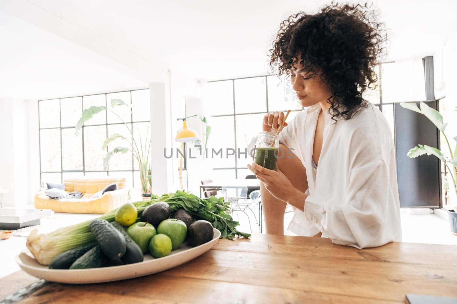 Young african american pretty woman relaxing in kitchen while having a green juice with bamboo straw in the morning. Home concept. Healthy lifestyle concept. Copy space.