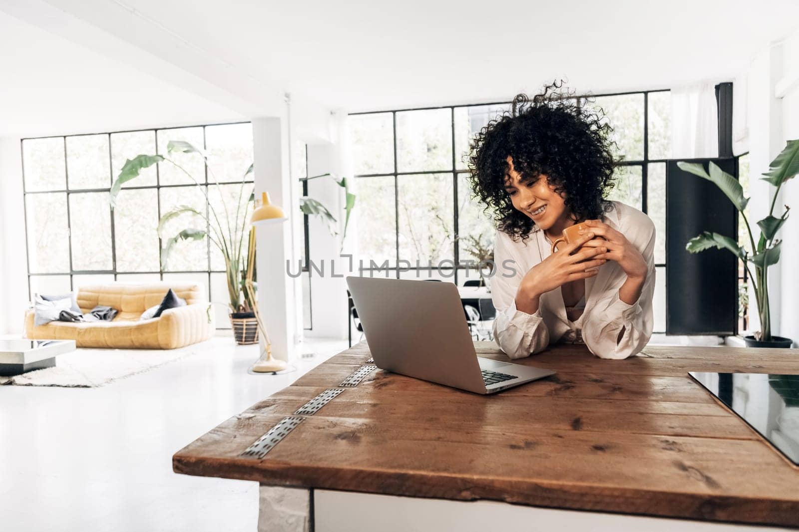 Young african american woman having a coffee in the morning looking laptop in bright loft kitchen by Hoverstock