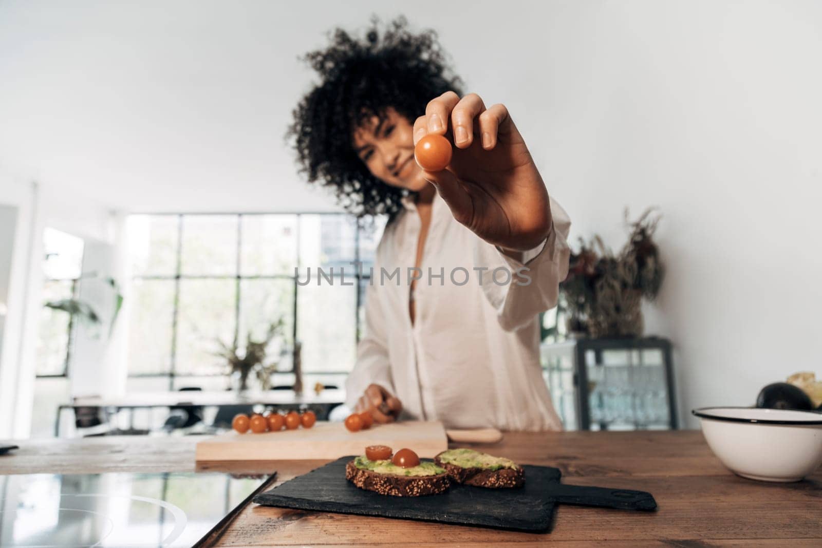 Woman showing a tomato looking at camera. Selective focus on hand and tomato by Hoverstock