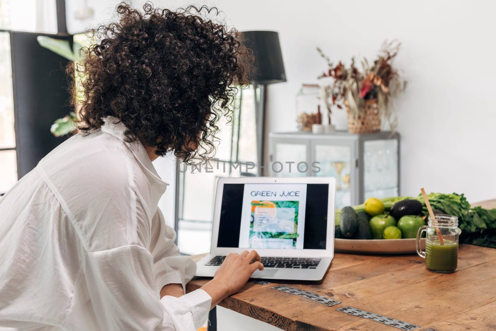 young mixed race woman looking recipe online on laptop. Green juice. Reusable bamboo straw. Kitchen counter top. Home concept. Technology concept. Health concept. Copy space