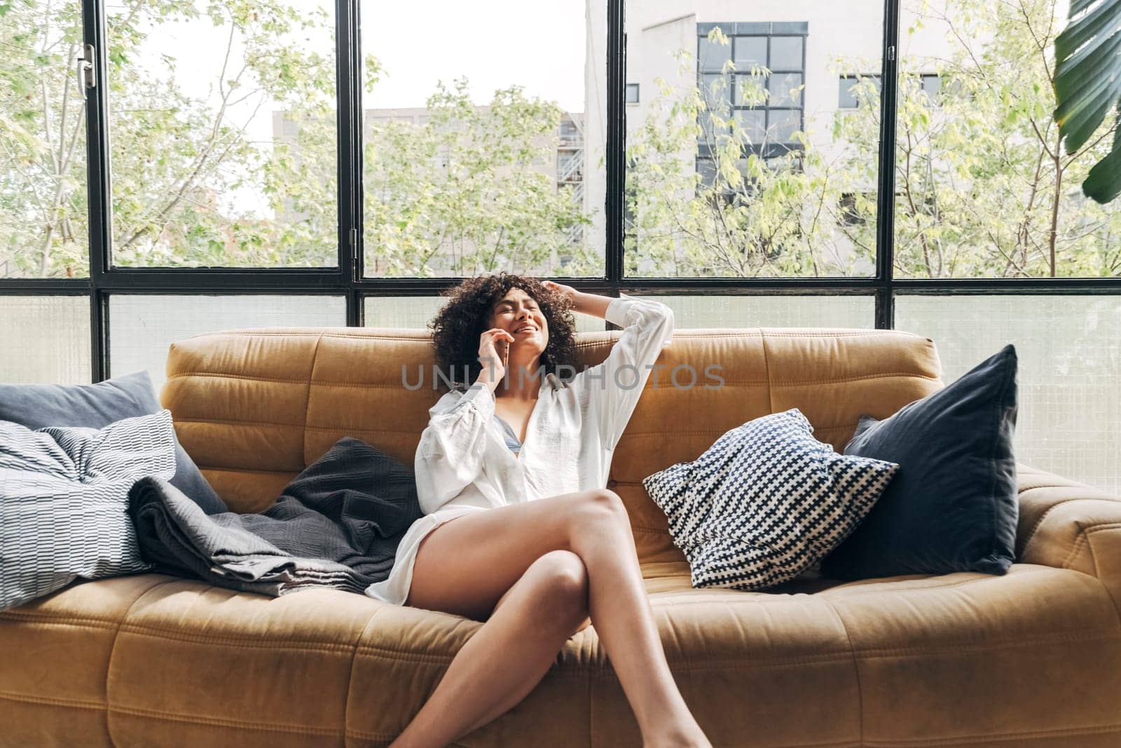Young African American woman relaxing on couch talking on cellphone in a bright loft living room. Home concept. Technology concept.