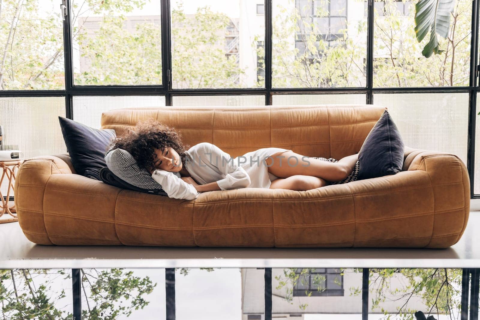Pensive young african american woman lying on a yellow sofa in a beautiful loft. Home concept.