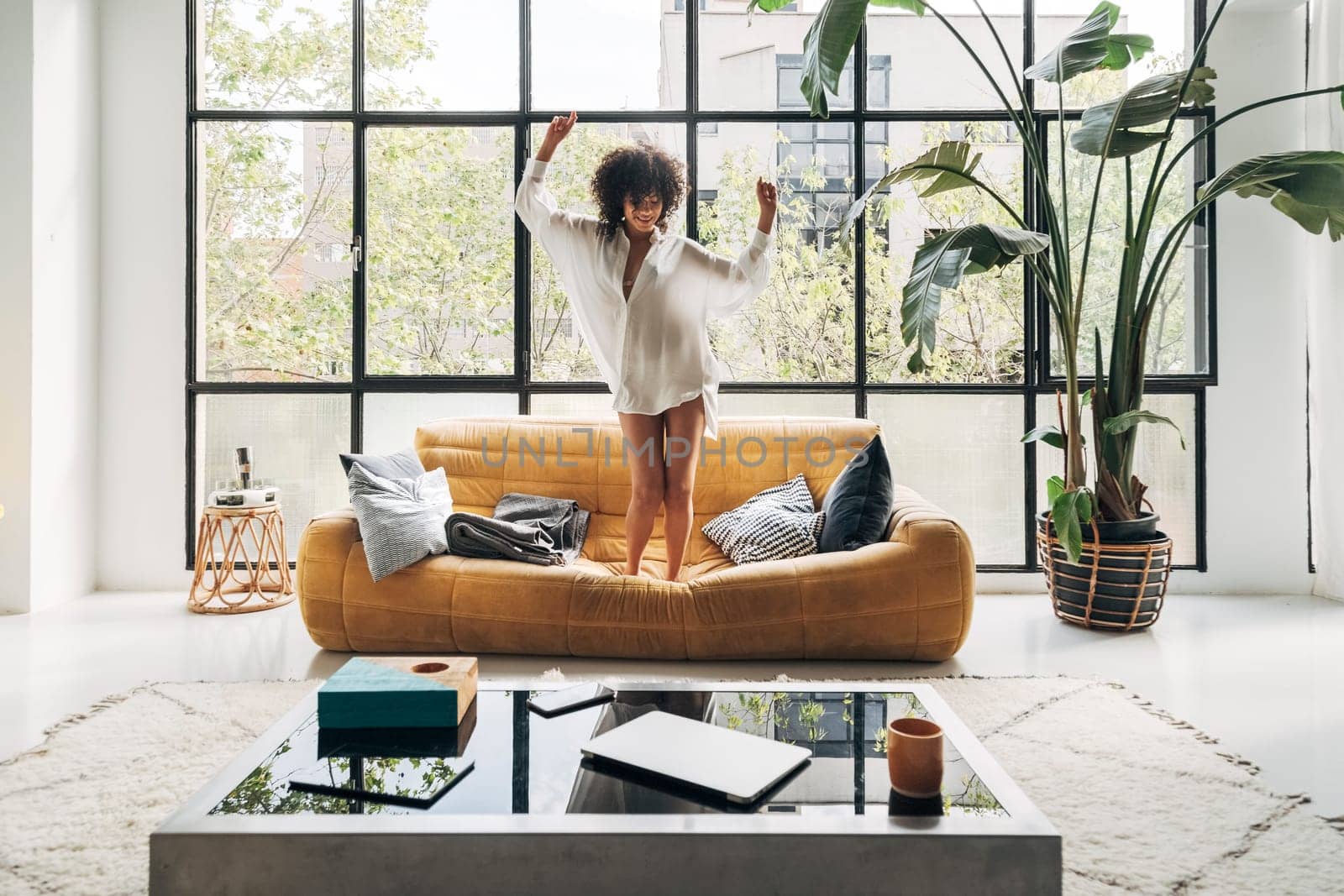 Young african american woman dancing to music on the couch in a bright living room . Home concept.