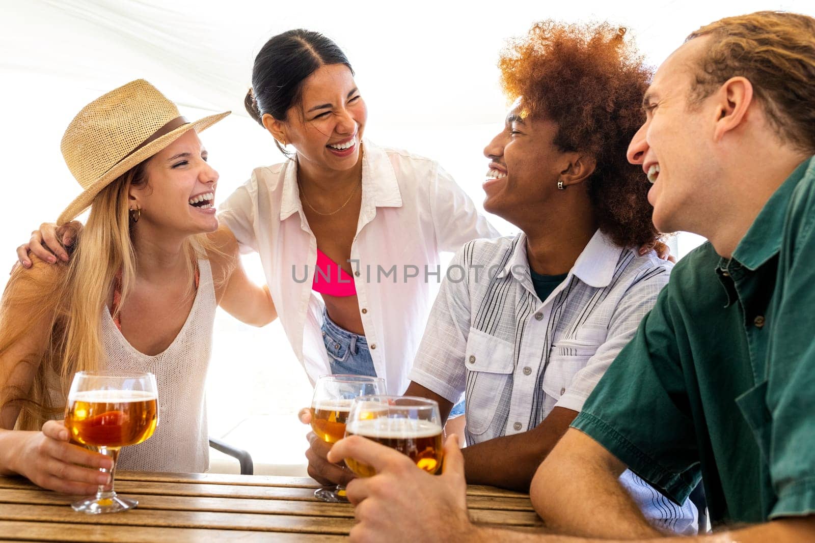 Young happy hispanic woman on vacation having fun with friends in beach bar while having beers together. by Hoverstock