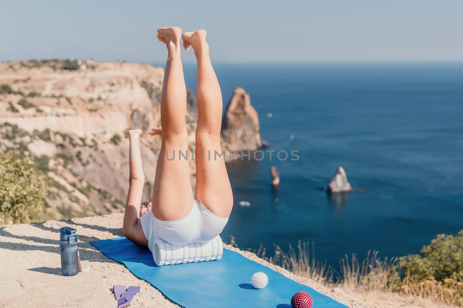 Woman sea pilates. Sporty happy middle aged woman practicing fitness on yoga mat with balls and roller near sea, smiling active female outside, enjoying healthy lifestyle, harmony and meditation. by panophotograph