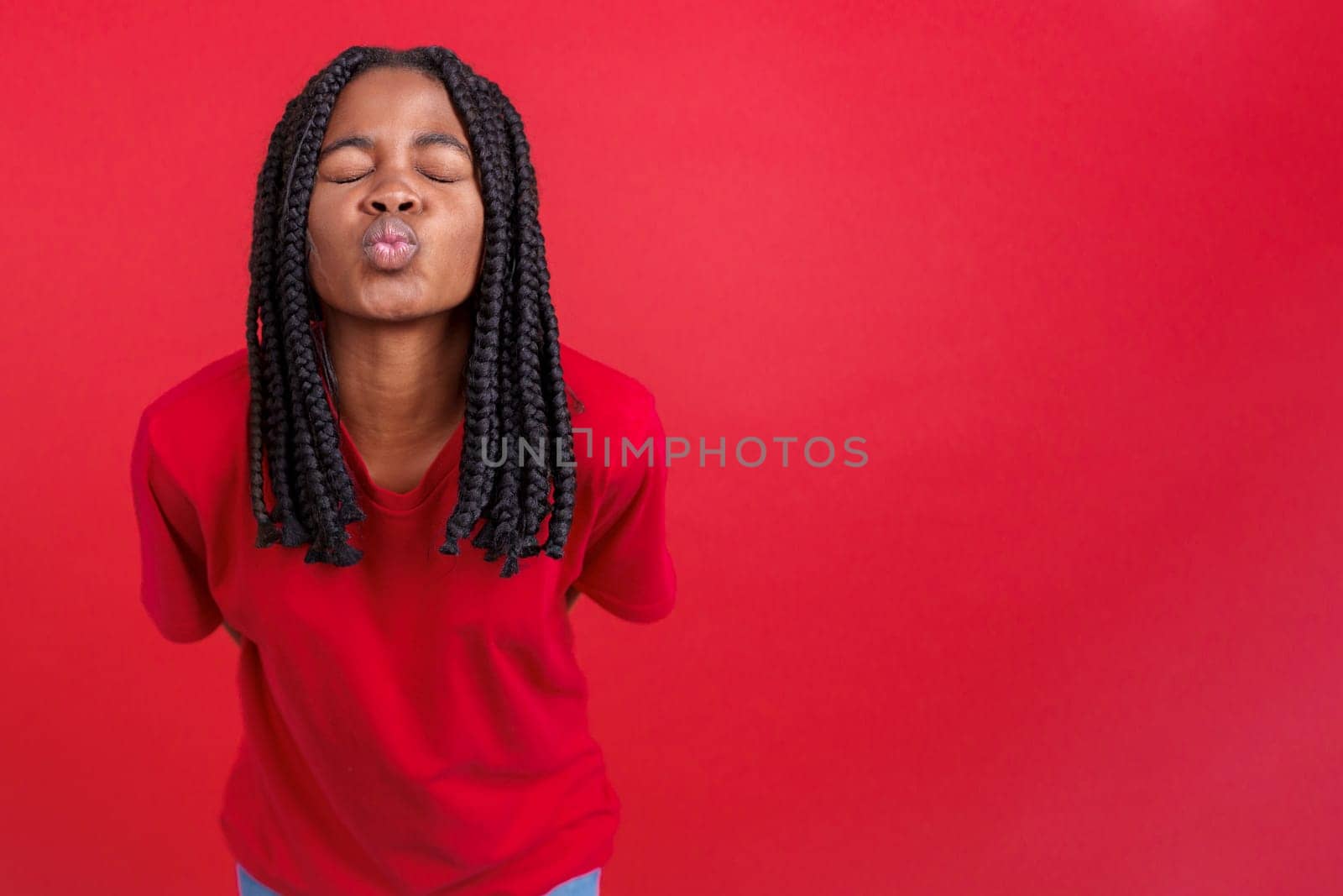 African woman blowing a kiss with eyes closed in studio with red background