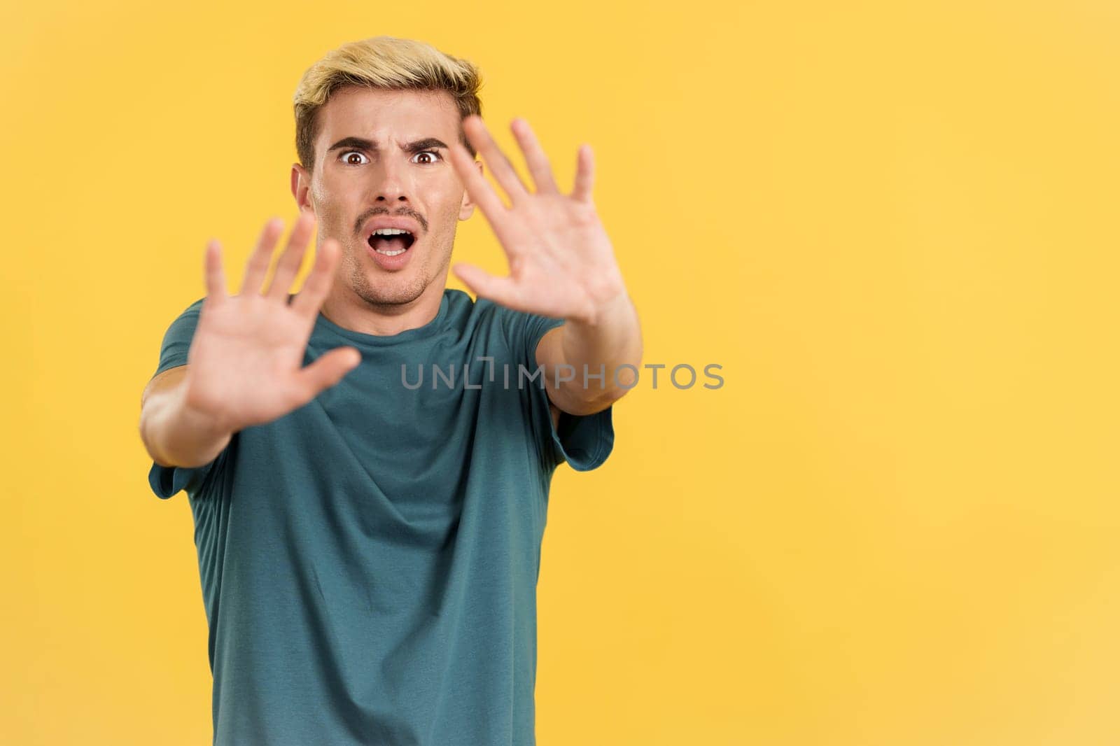 Gay man gesturing with the hands in fear in studio with yellow background