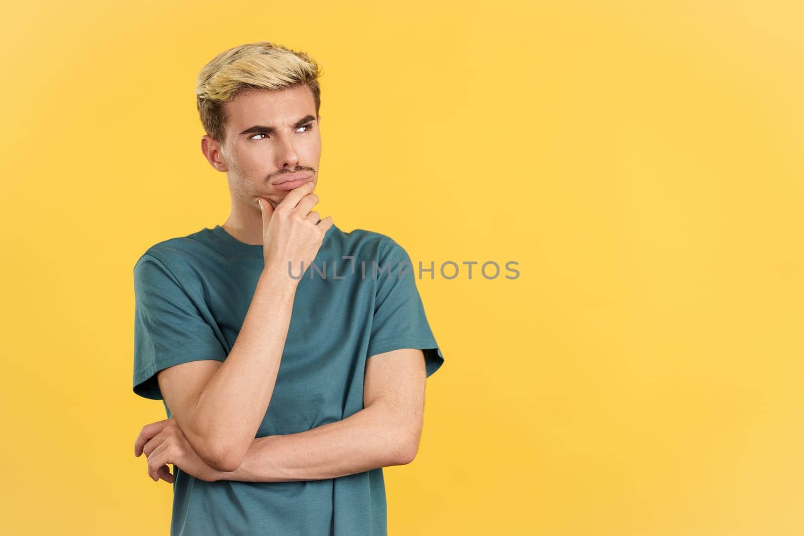 Gay man with hand on face and thoughtful expression in studio with yellow background