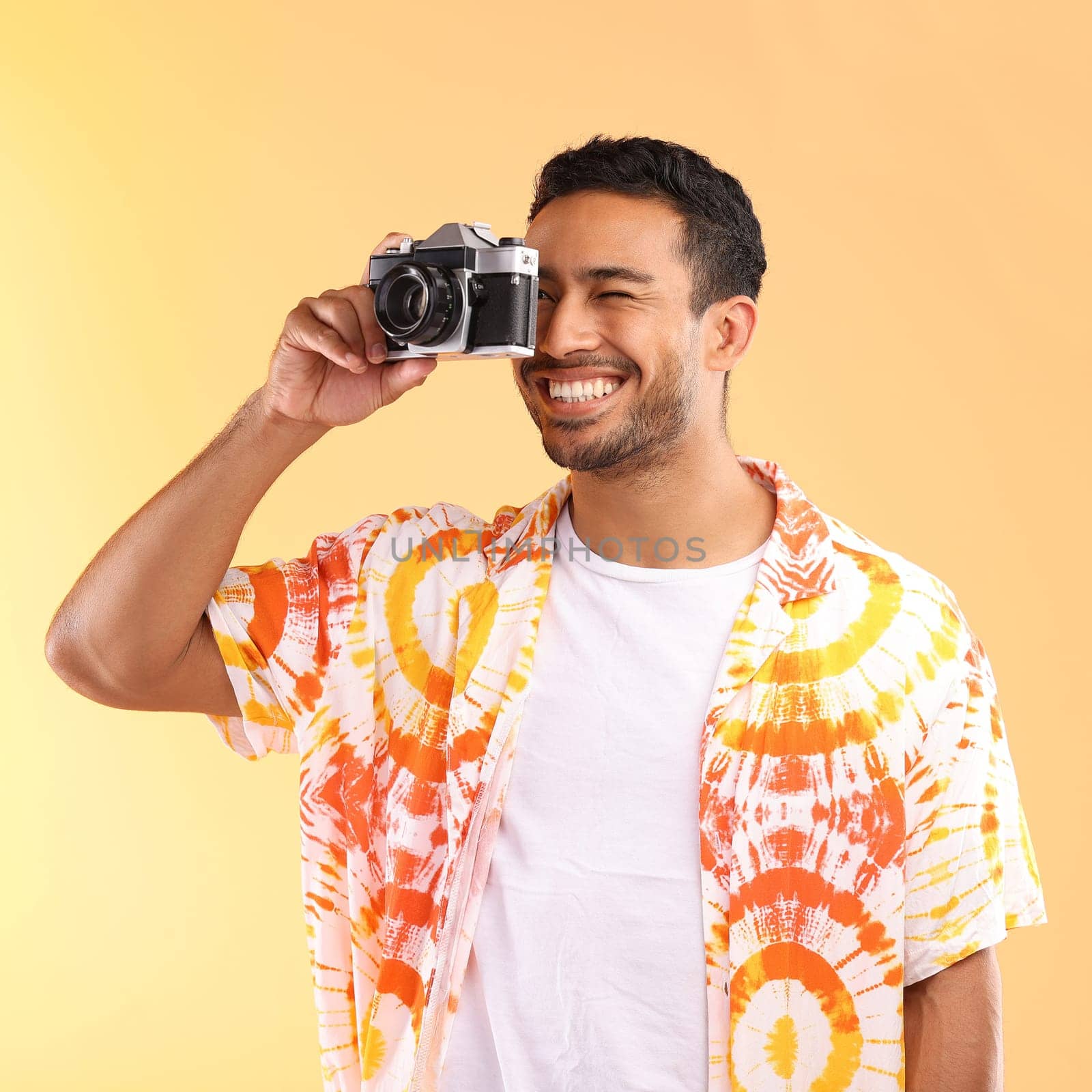Photographer, camera and man taking pictures in studio isolated on an orange background. Travel, vacation and male model holding camcorder technology for taking photo for happy memory on holiday