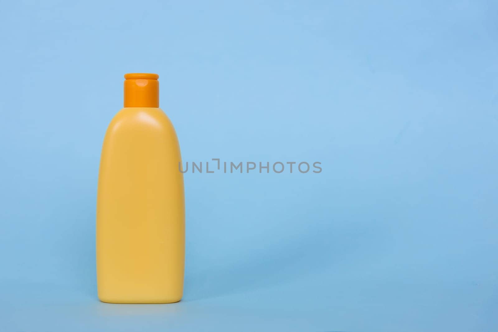 Mock up of a yellow plastic bottle with a cosmetic liquid product on a blue background. Space for logo.