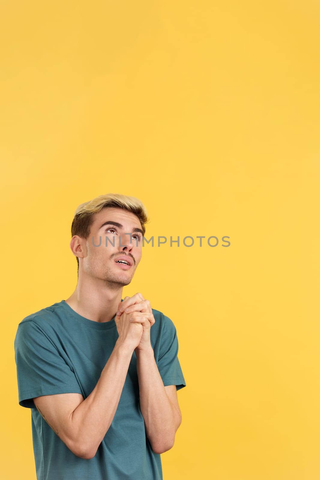 Gay man looking up while praying with folded hands in studio with yellow background