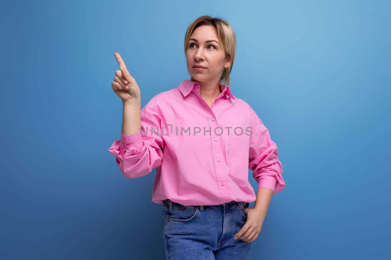 stylish young blond businesswoman in a pink shirt and jeans gesticulates inspiredly and talks about the idea of a business on a studio background with copy space.