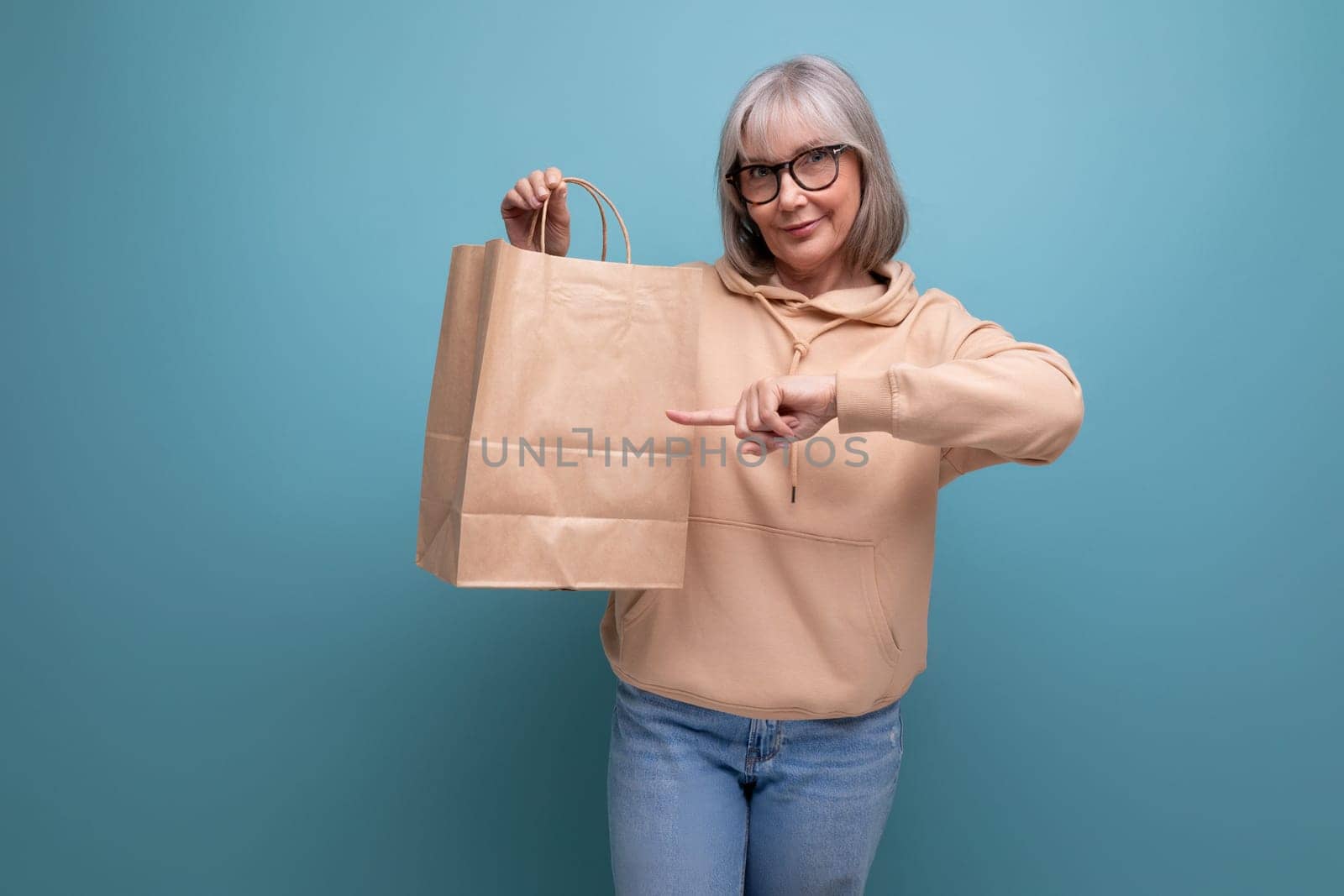 mature 60s business woman with gray hair holding craft shopping bag on studio background with copy space.