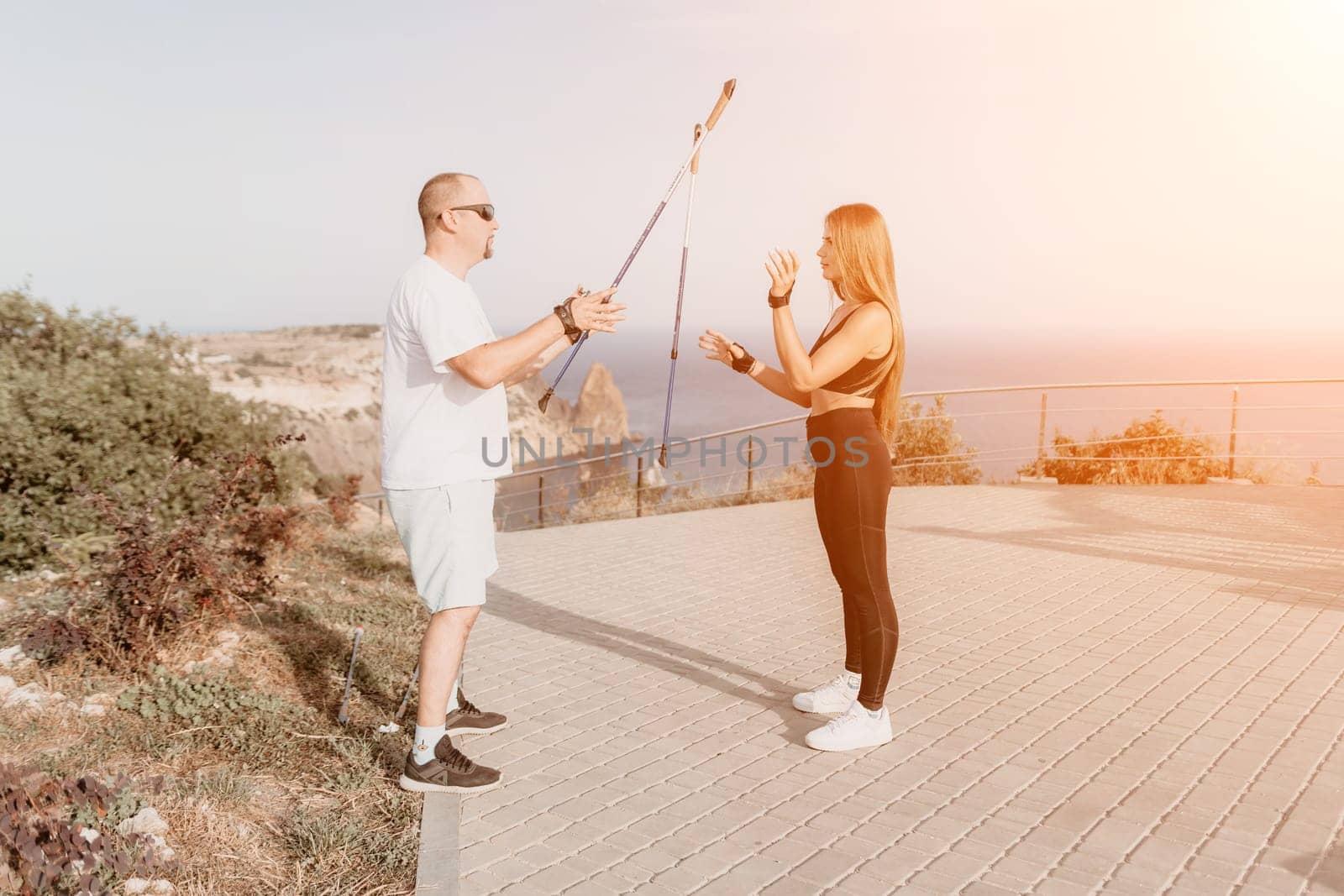 Happy Middle aged couple or friends practicing nordic walking in park near sea. Mature couple with trekking poles walking, practicing Nordic walking outdoors. Aging youthfully and sport concept.