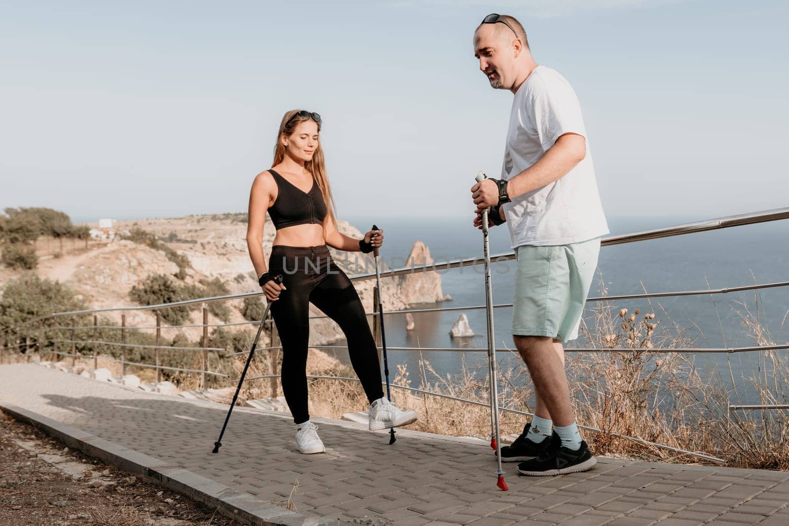 Happy Middle aged couple or friends practicing nordic walking in park near sea. Mature couple with trekking poles walking, practicing Nordic walking outdoors. Aging youthfully and sport concept.