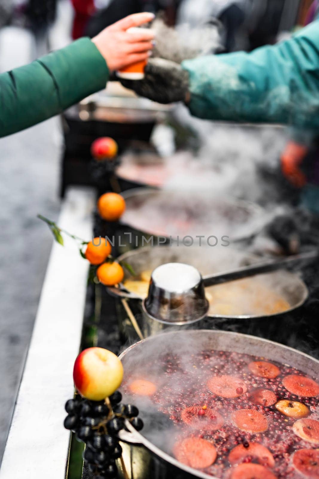 Person buy hot fruit and berries mulled winebeverage at street food market. Fresh drinks in pots at fair outdoors