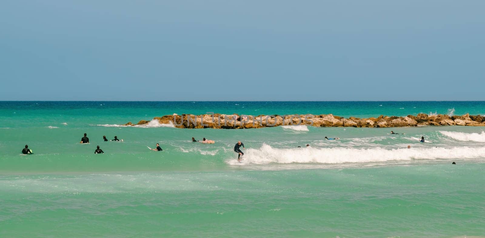 Surfing on a water board. A group of people surfers ride the waves in the ocean. Athletes in training with a coach learn to catch waves. Netanya, Israel. May 23, 2023.