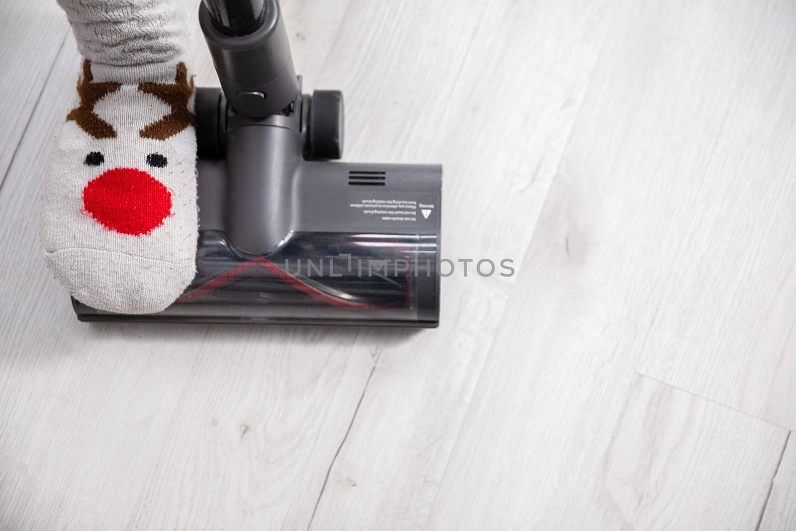 An overhead view of one foot trampling the end of a vacuum cleaner. Keeping things tidy by cleaning the floorboards frequently.