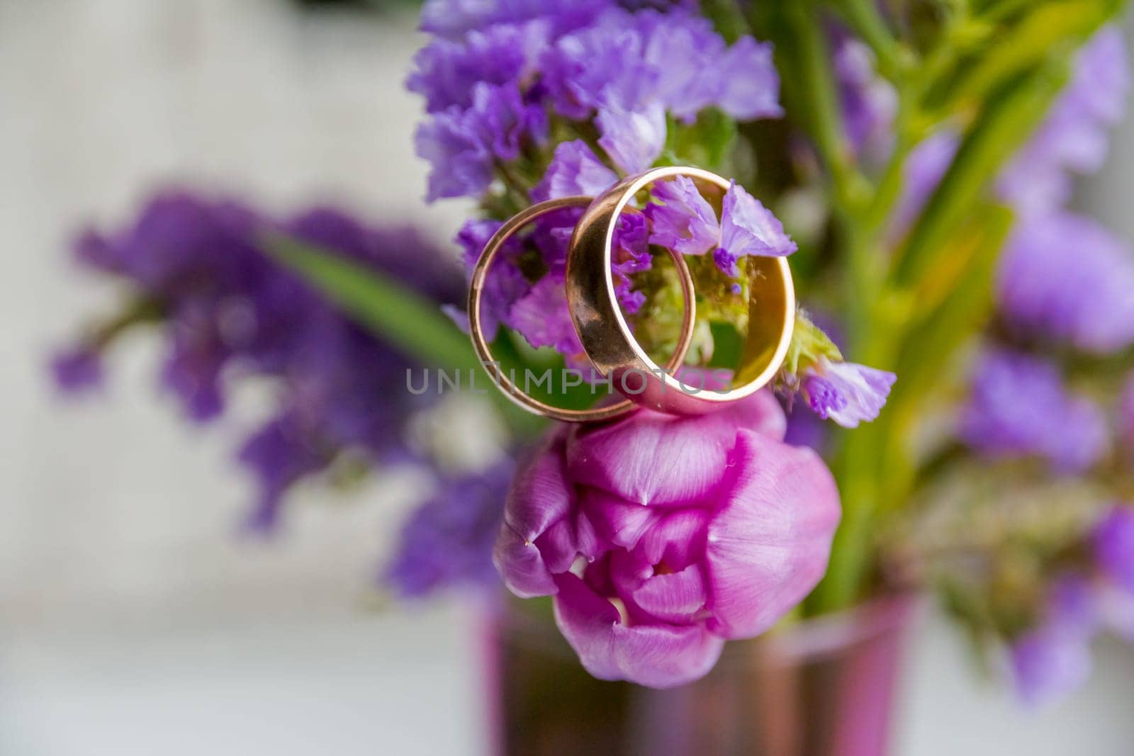 Wedding concept: bouquet of multicolored tulips and two rings on white satin fabric