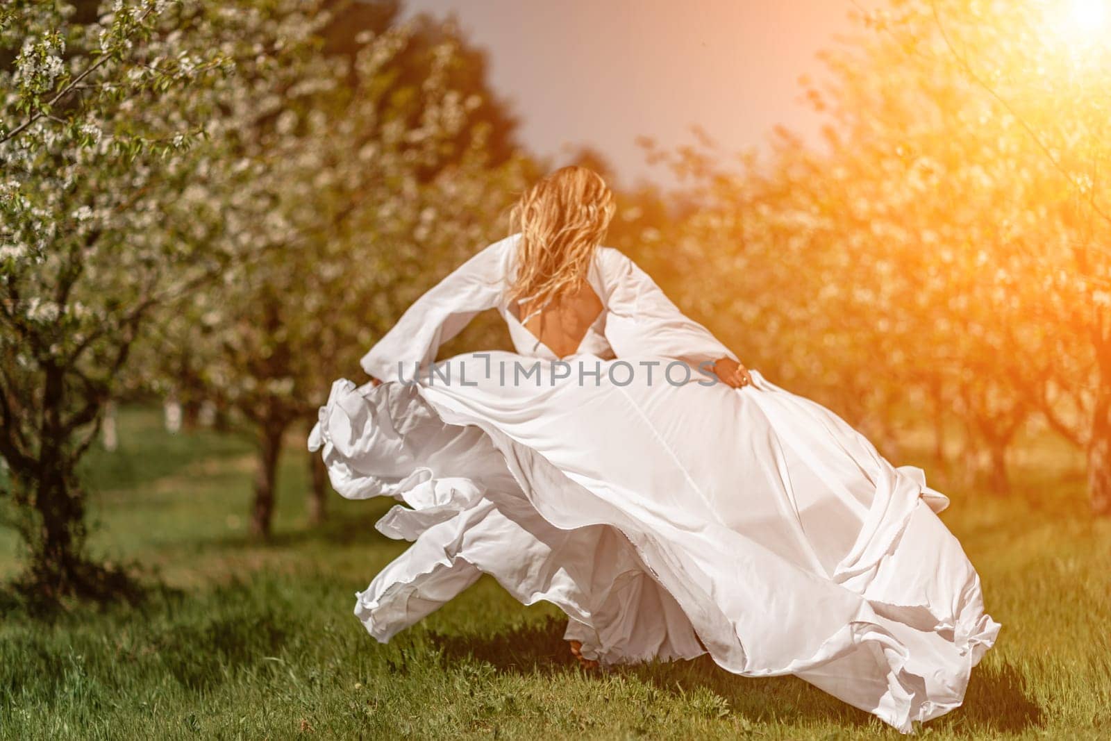 Woman white dress park. A woman in a white dress runs through a blossoming cherry orchard. The long dress flies to the sides, the bride runs rejoicing in life