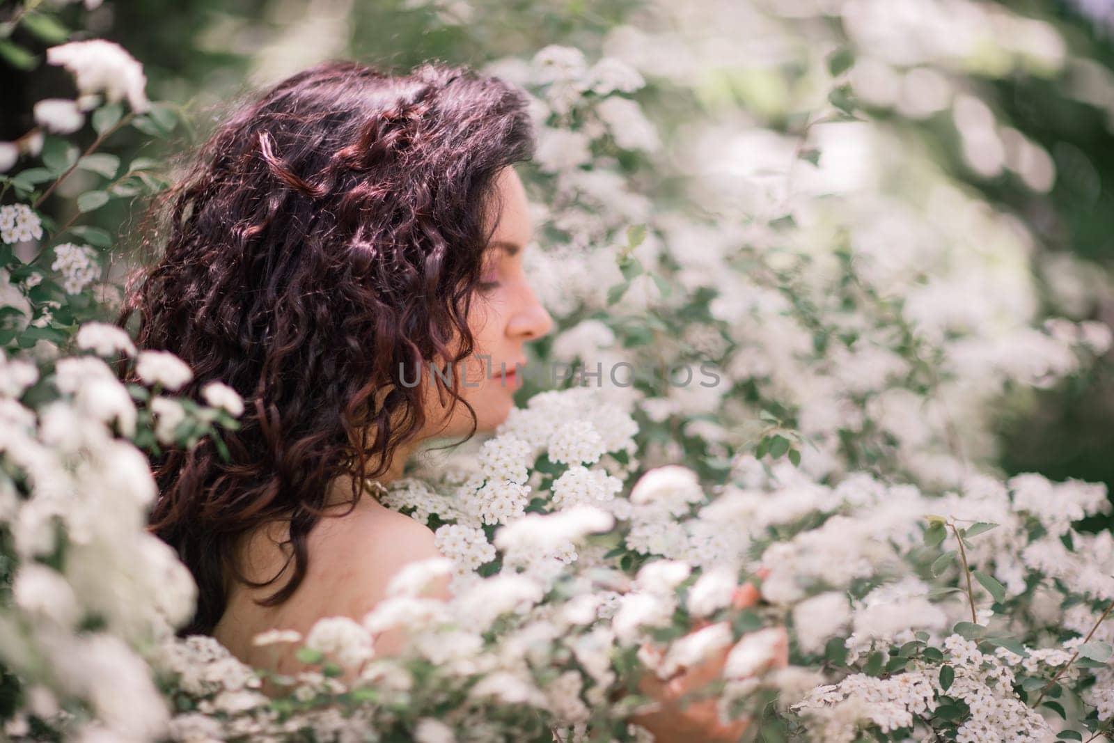 Woman spirea flowers. Portrait of a curly happy woman in a flowering bush with white spirea flowers. by Matiunina