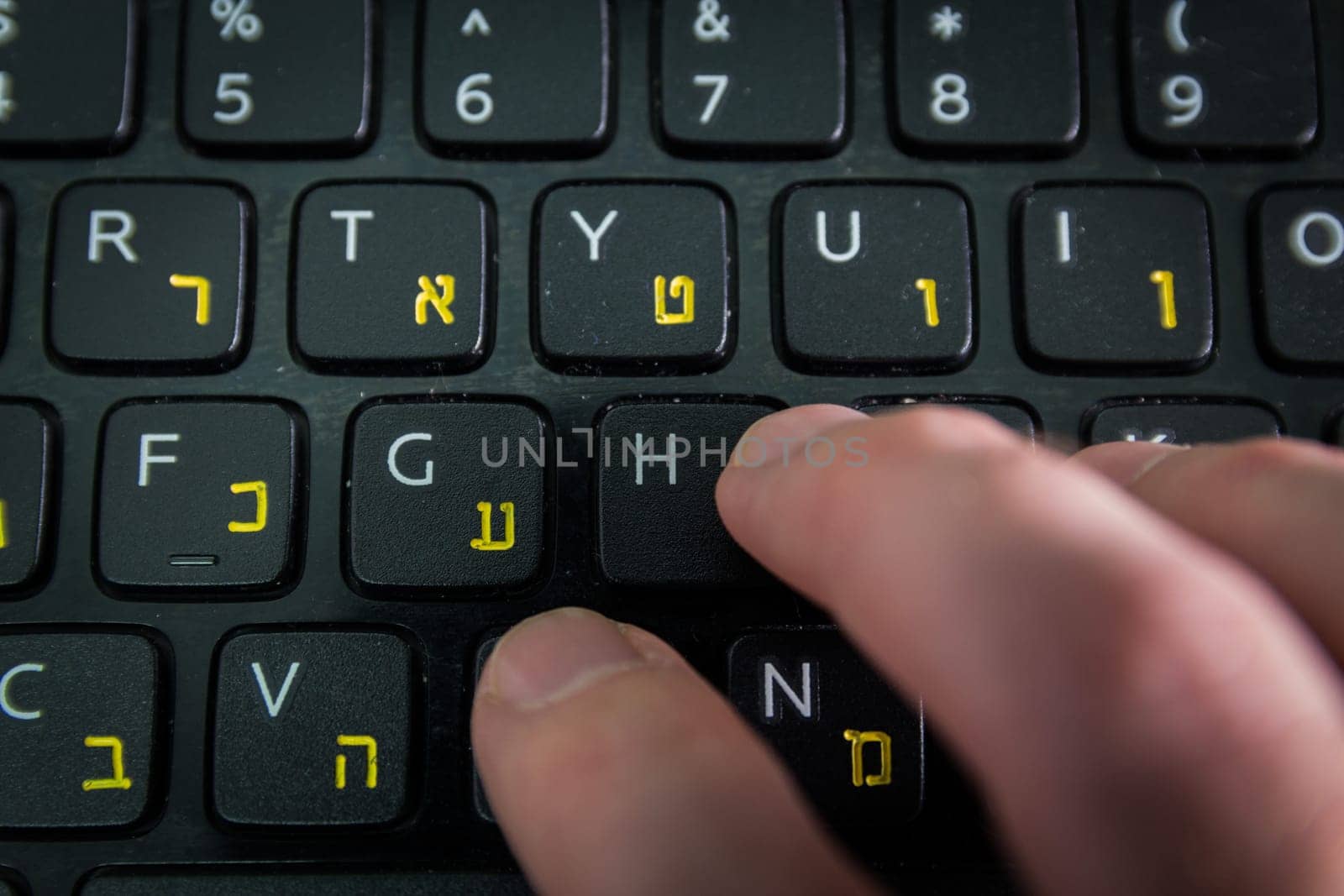 Man typing on a keyboard with letters in Hebrew and English - Laptop keyboard - Top View - Close up_Dark atmosphere