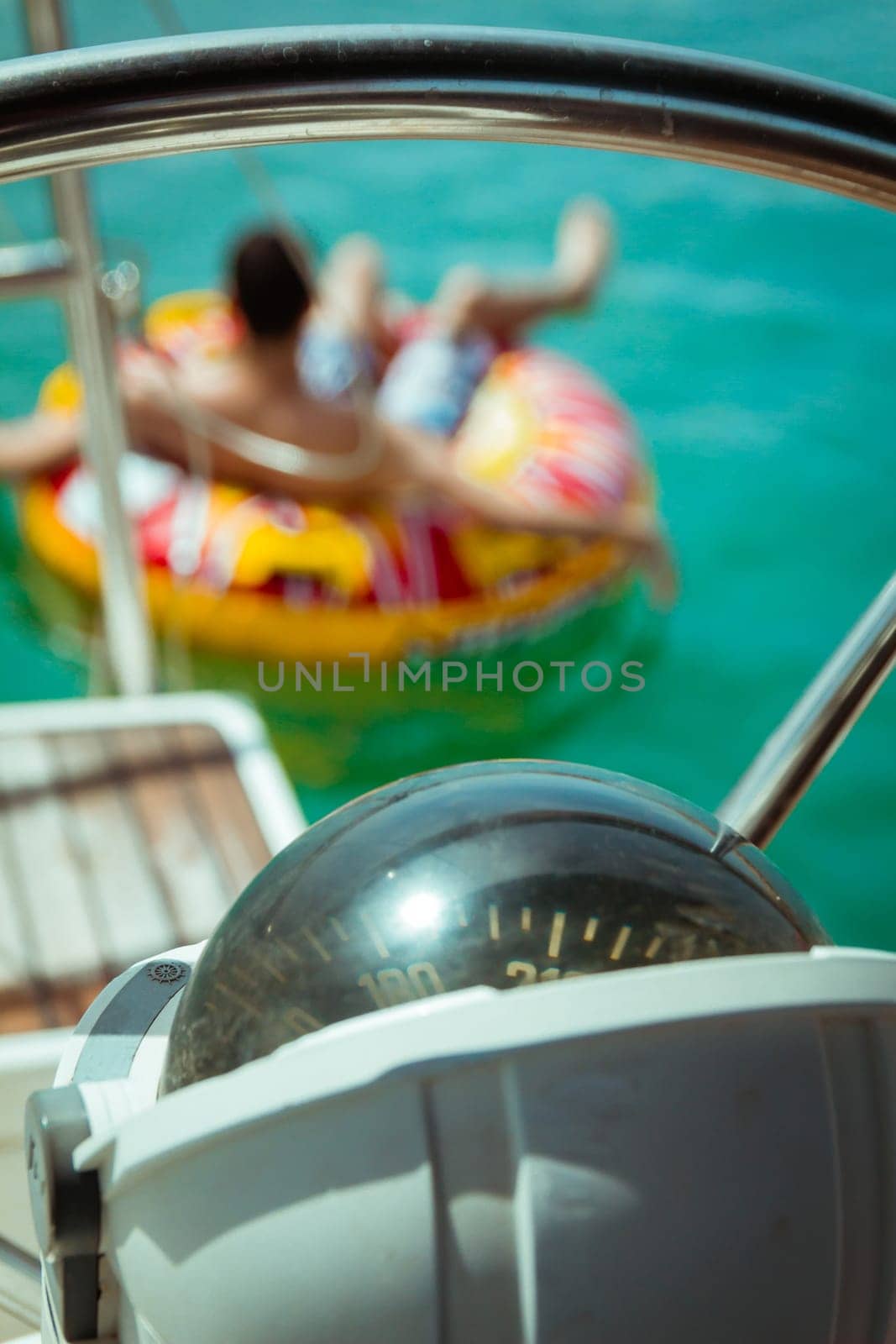 Compass on a yacht boat. In the background there is a man floating in inflatable ring.