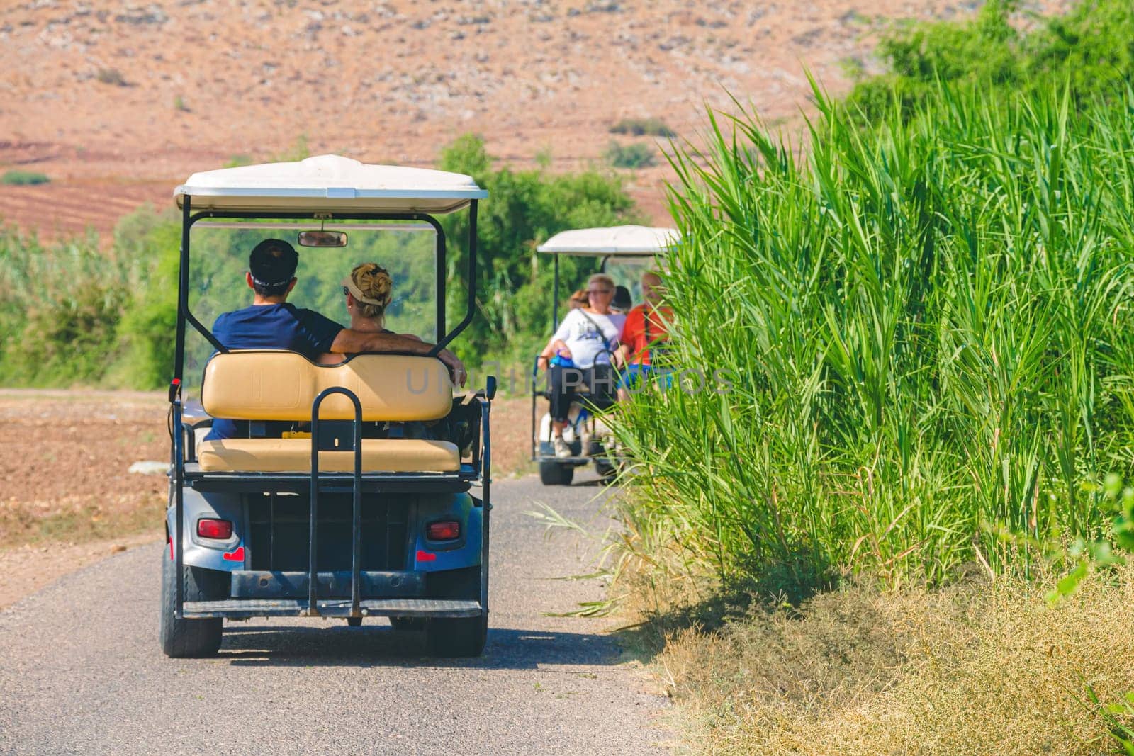 Backshot of Israeli people driving on electric golf cart while traveling in the countryside of the Israeli Hula Valley in summer day.