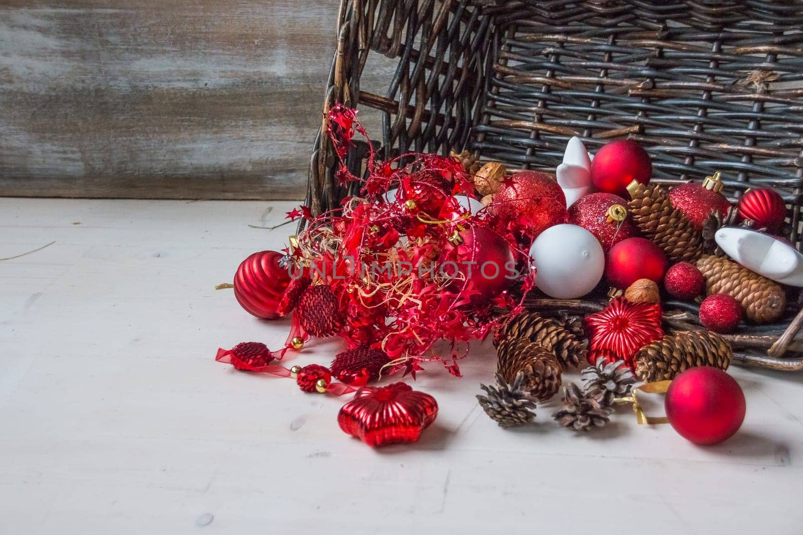 Christmas basket with champagne bottle and glasses, gifts with red satin ribbon, candy canes, pine cones, golden garlands on white wooden background