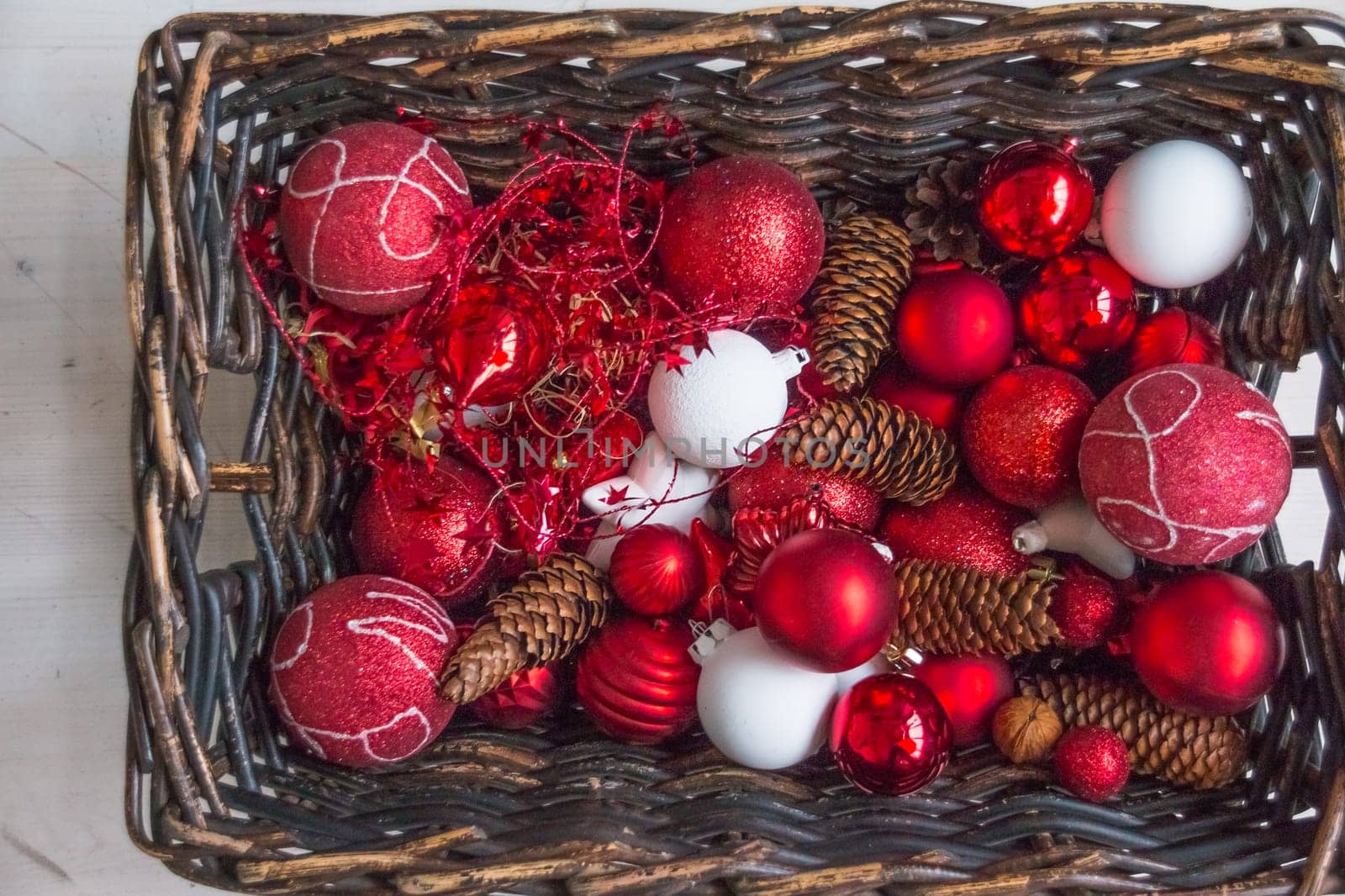 Christmas basket with champagne bottle and glasses, gifts with red satin ribbon, candy canes, pine cones, golden garlands on white wooden background