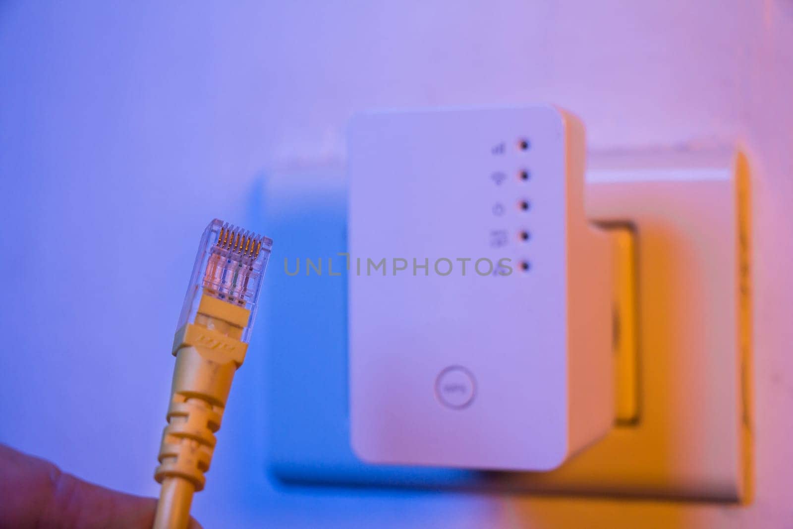 Closeup of ethernet cable. WiFi extender device in electrical socket on the wall on the background. The device is in access point mode that help to extend wireless network in home or office.