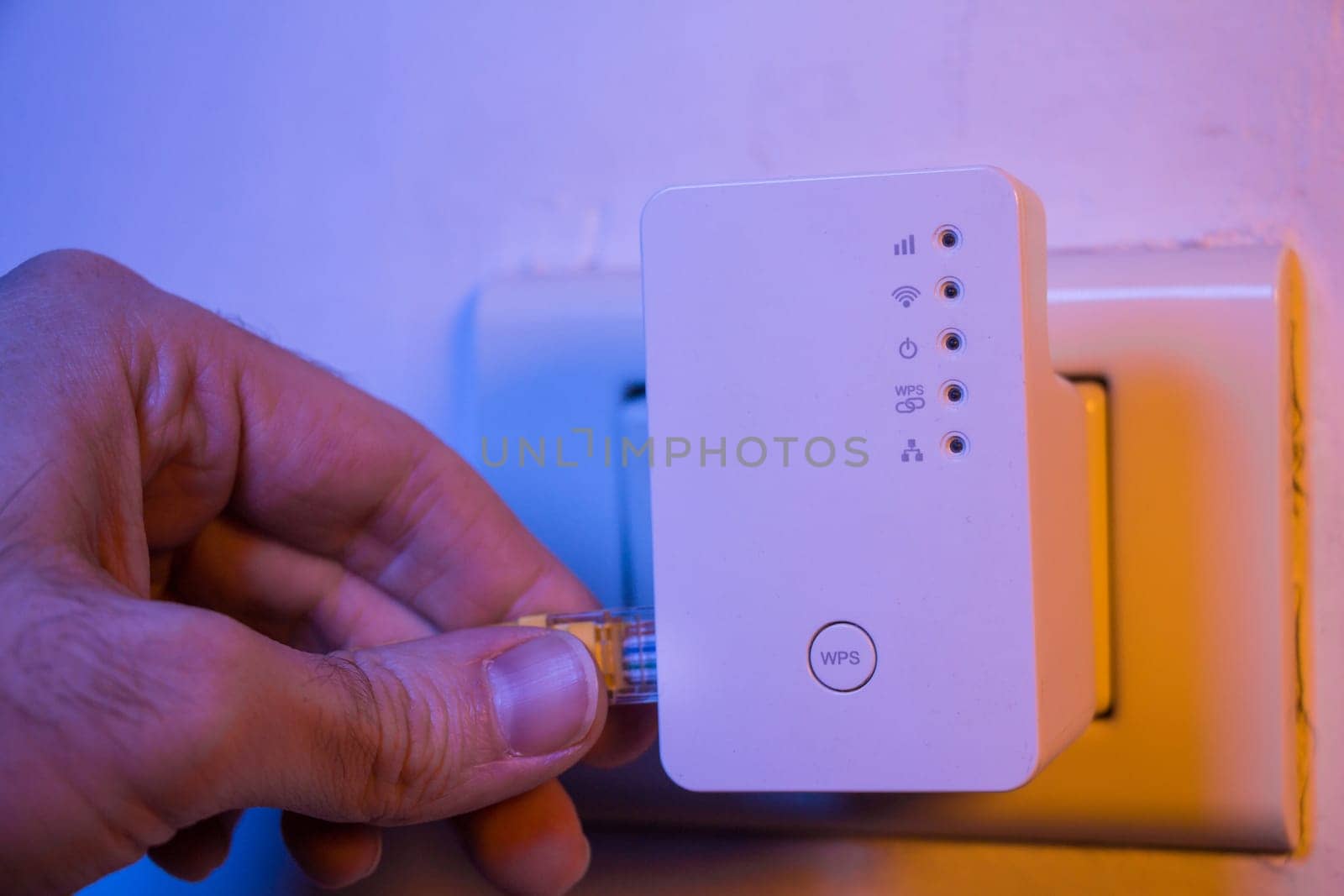 Man insert ethernet cable into WiFi extender device which is in electrical socket on the wall. The device is in access point mode that help to extend wireless network in home or office.