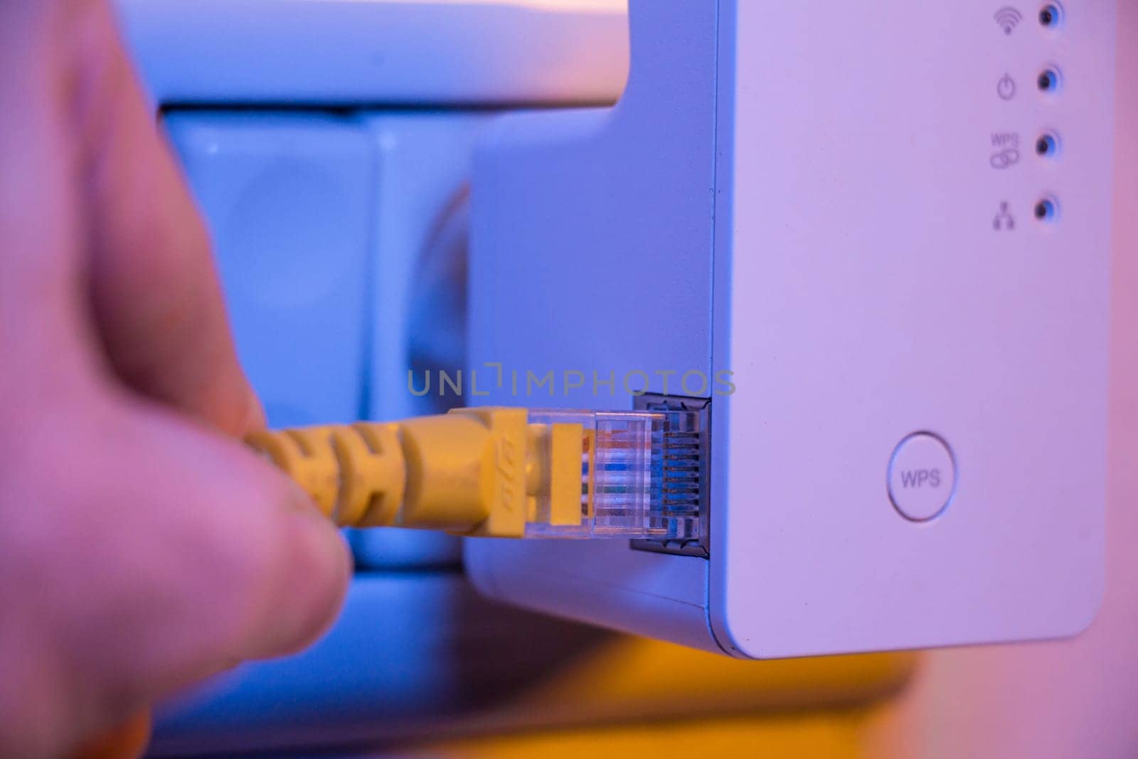 Man insert ethernet cable into WiFi extender device which is in electrical socket on the wall. The device is in access point mode that help to extend wireless network in home or office.