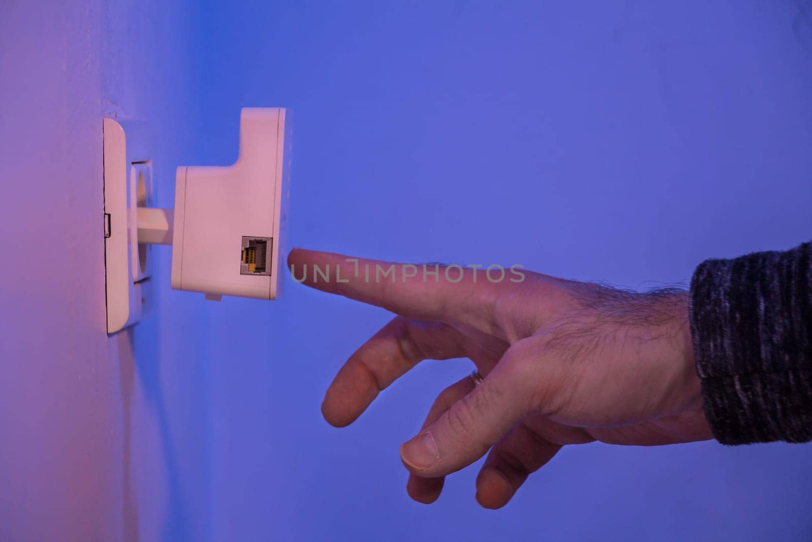 Man press with his finger on WPS button on WiFi repeater which is in electrical socket on the wall by wavemovies