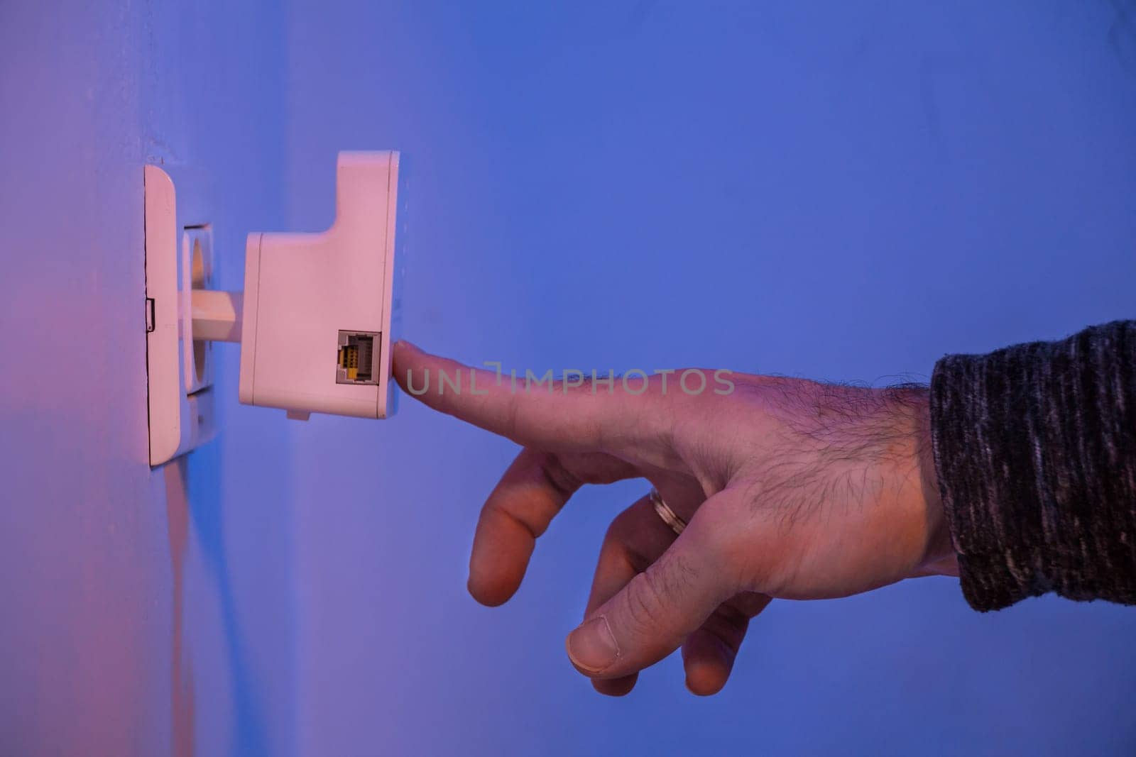Man press with his finger on WPS button on WiFi repeater which is in electrical socket on the wall by wavemovies