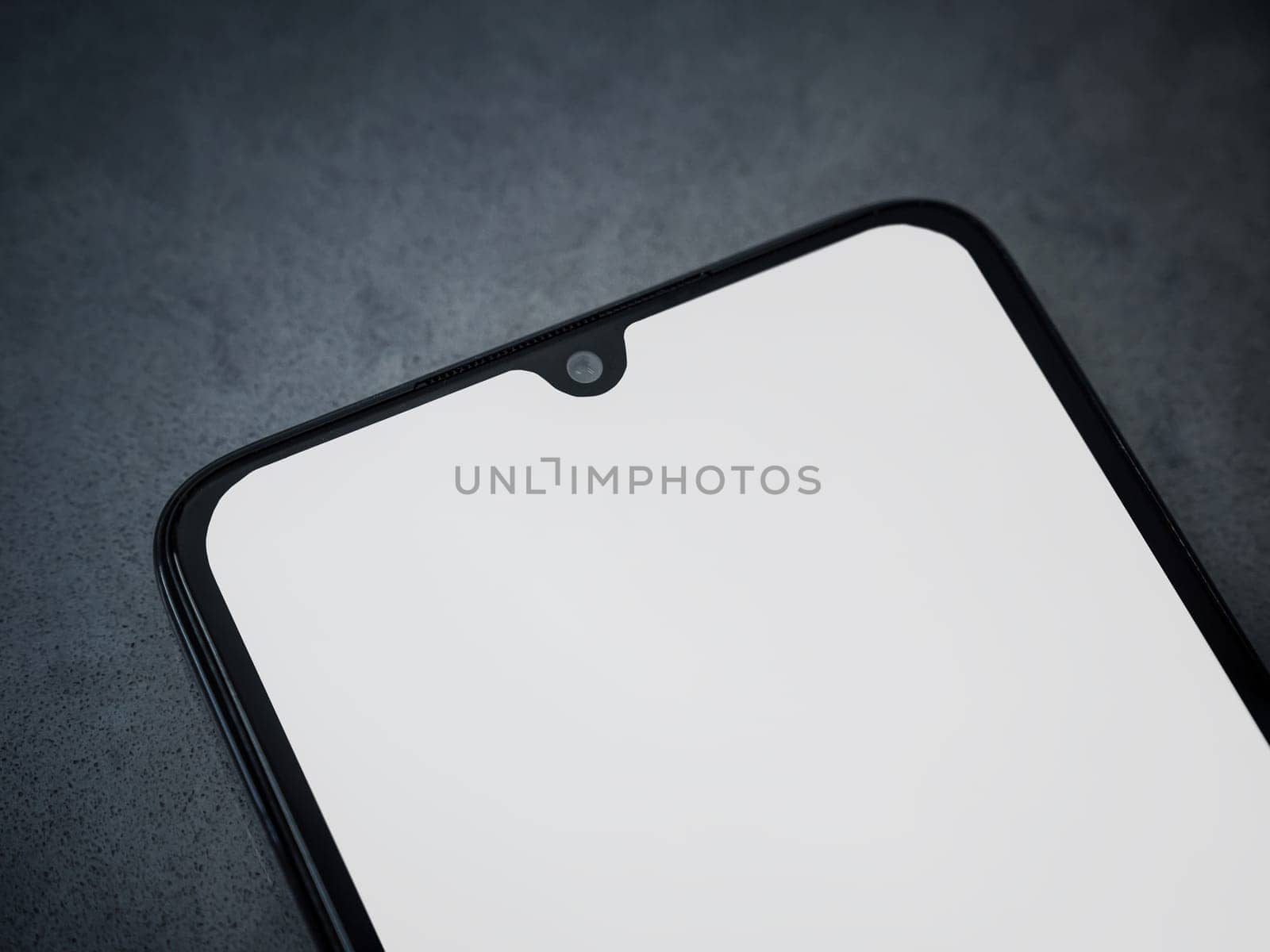 Black mobile smartphone mockup lies on the surface with a blank screen isolated on a dark marble stone background. Top view close up with selective focus and copy space, cut in the middle.