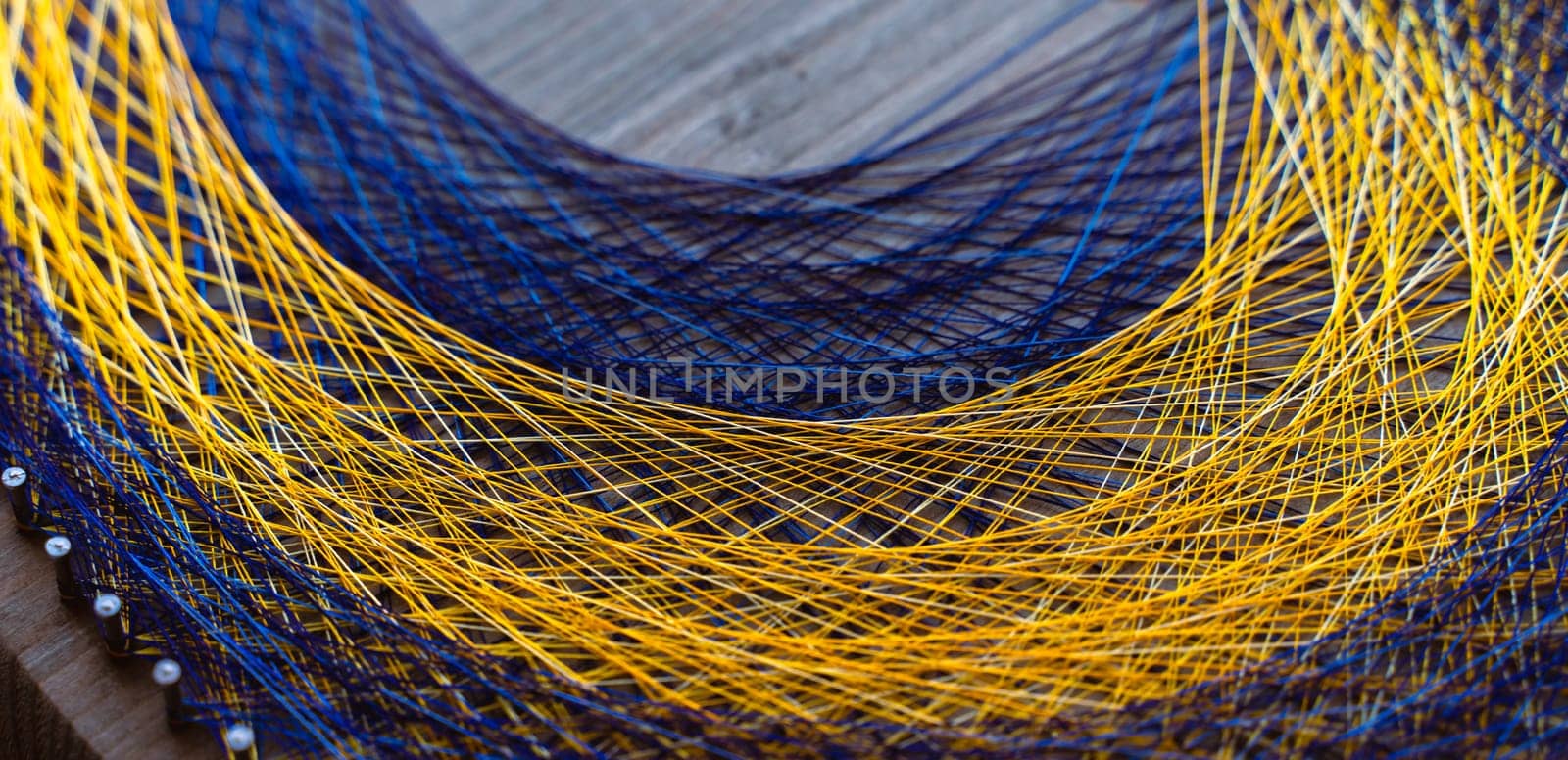 Colored thread mandala on a wooden board with nails. Mandala Moon Harmony Sun esotericism and psychology pictures from yellow and blue silk threads. by Matiunina