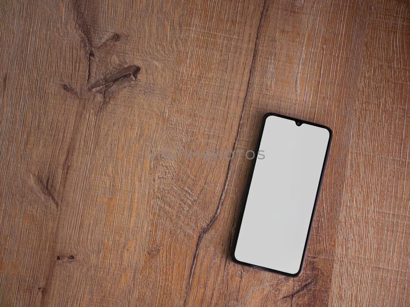 Black mobile smartphone mockup lies on the surface with blank screen isolated on wooden background by wavemovies